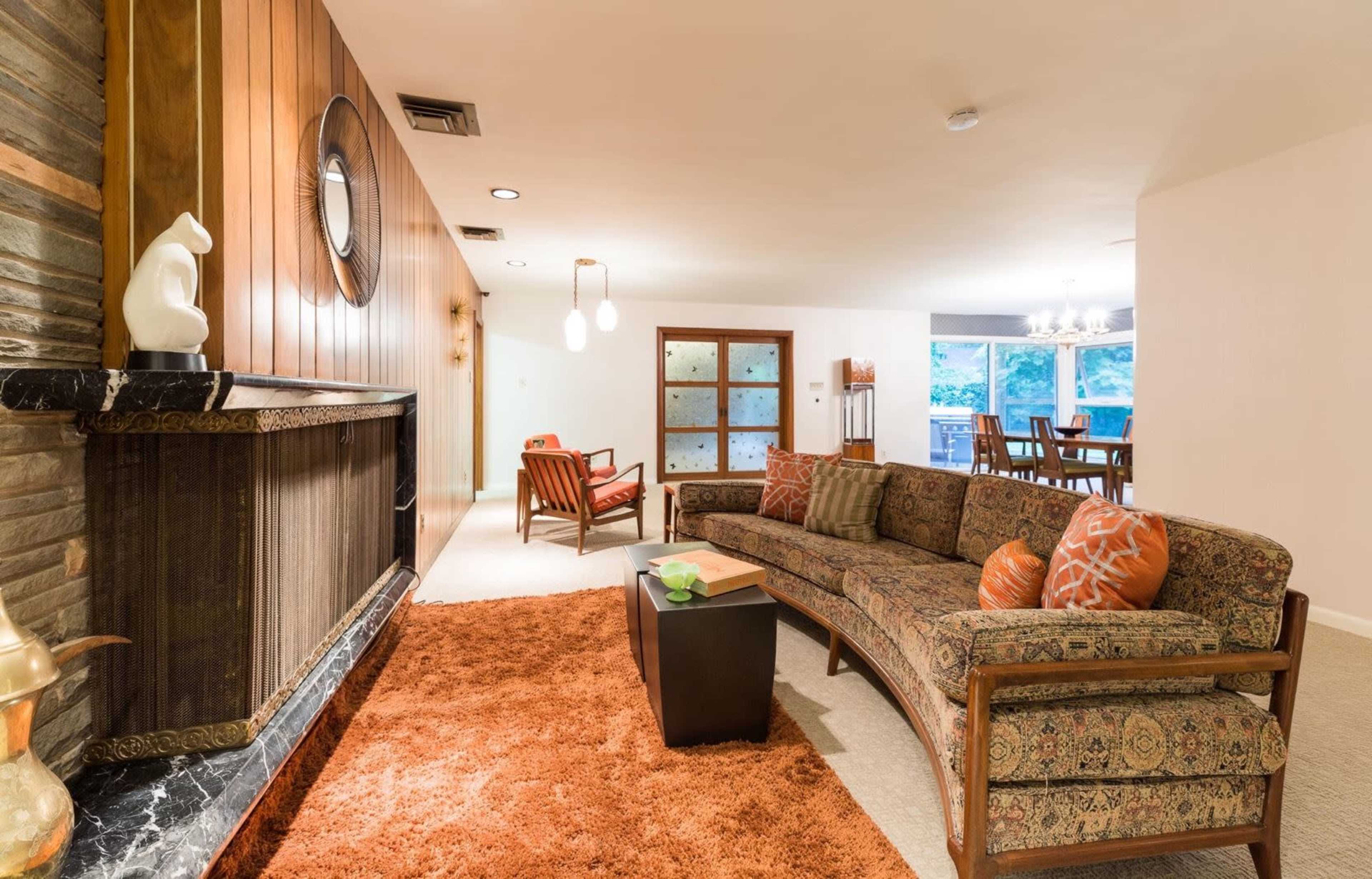 A spacious living room features a curved sofa, a stone fireplace, and a dining area in the background.