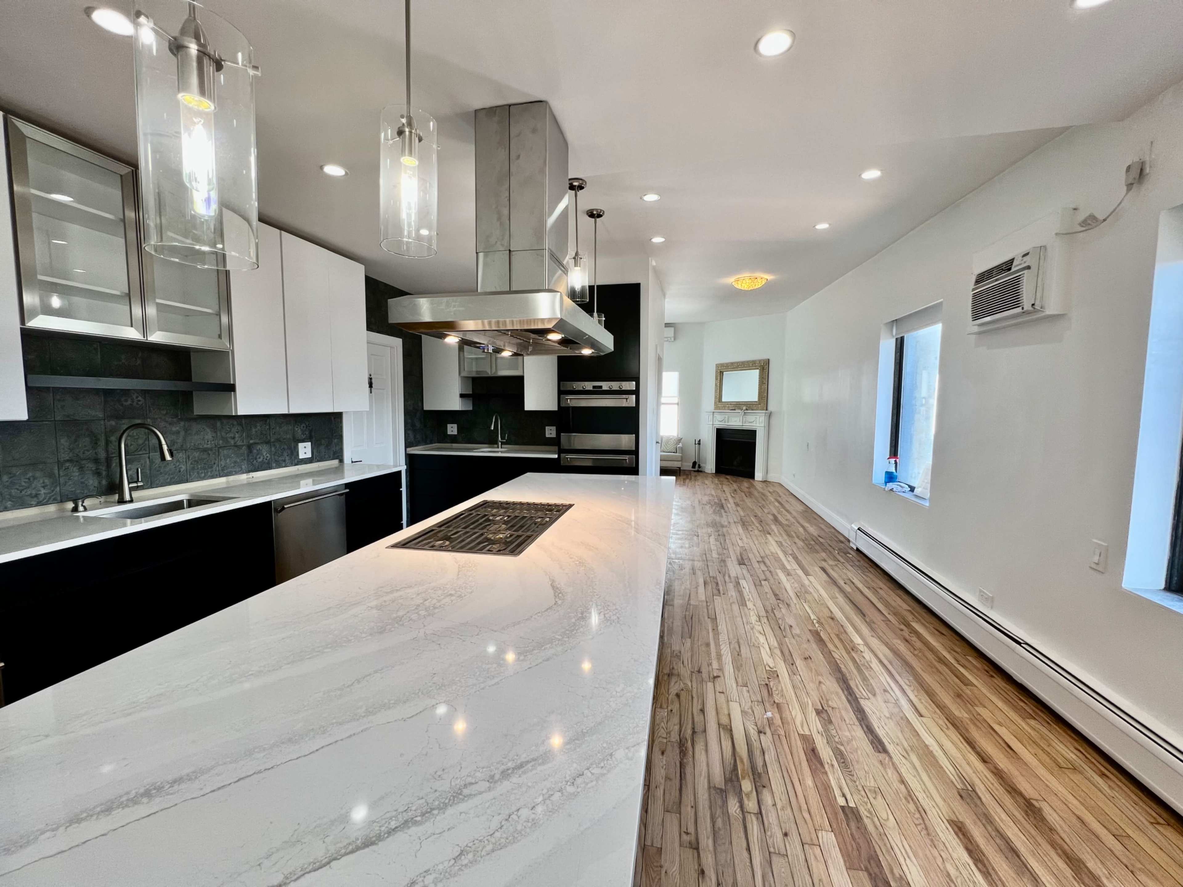 The image shows a modern kitchen featuring a large island with a marble countertop, stainless steel appliances, and wooden flooring.