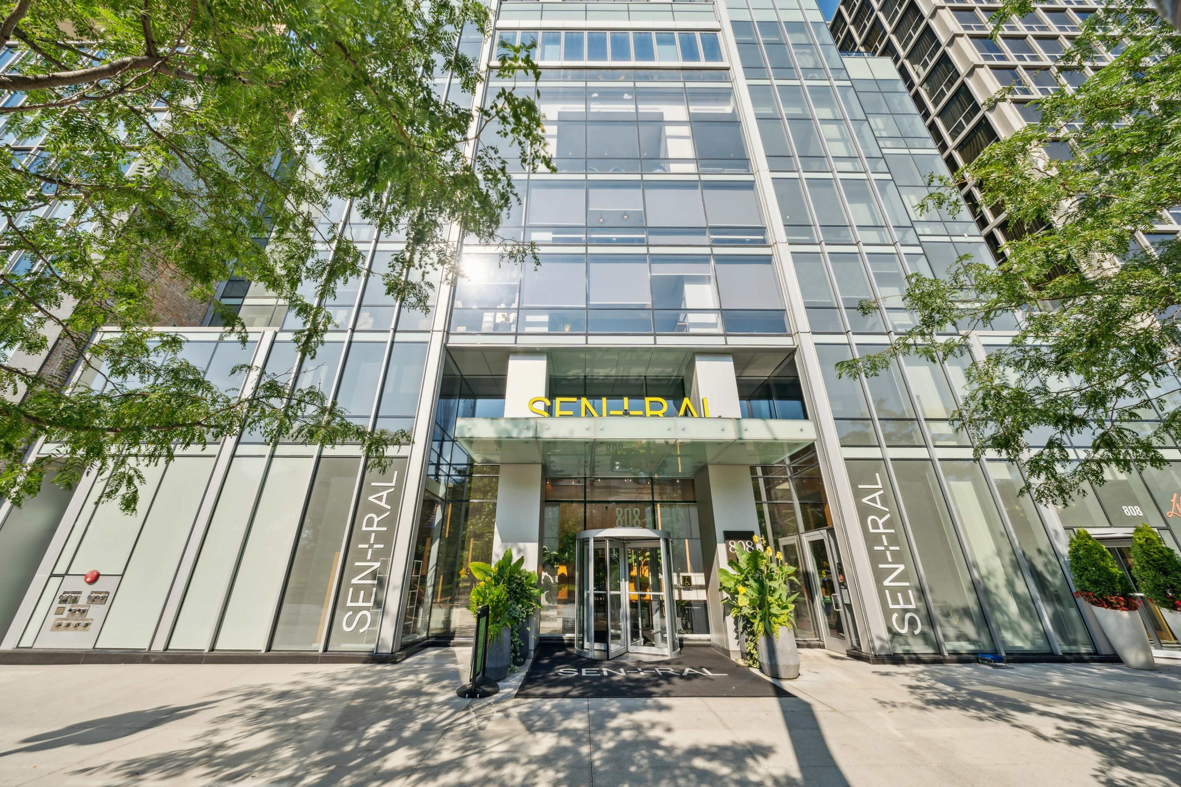 The image shows the entrance of a modern glass-fronted building with the name "SEN-TRAL" prominently displayed above the entrance.