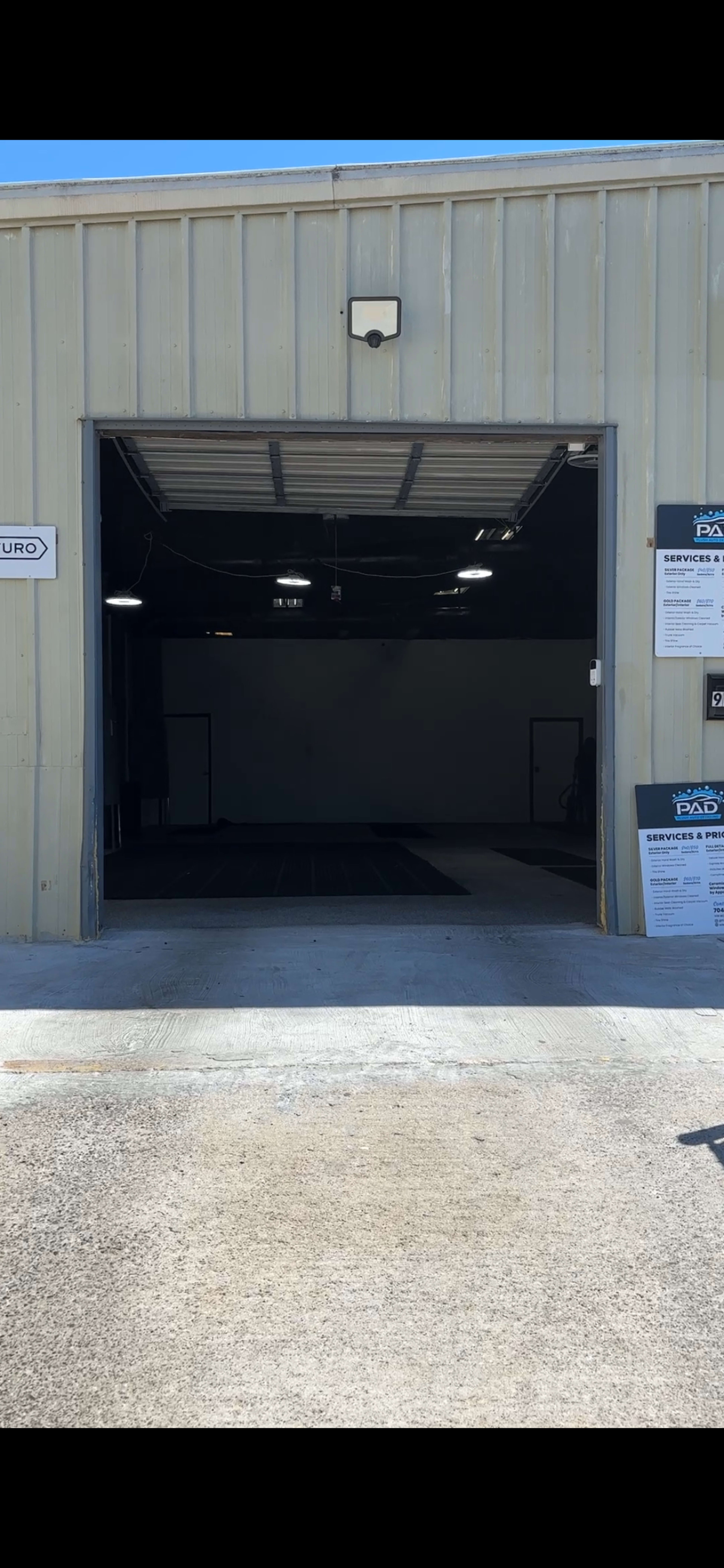 The image shows a large open garage door leading into a dimly lit service area, with signage visible on both sides of the entrance.