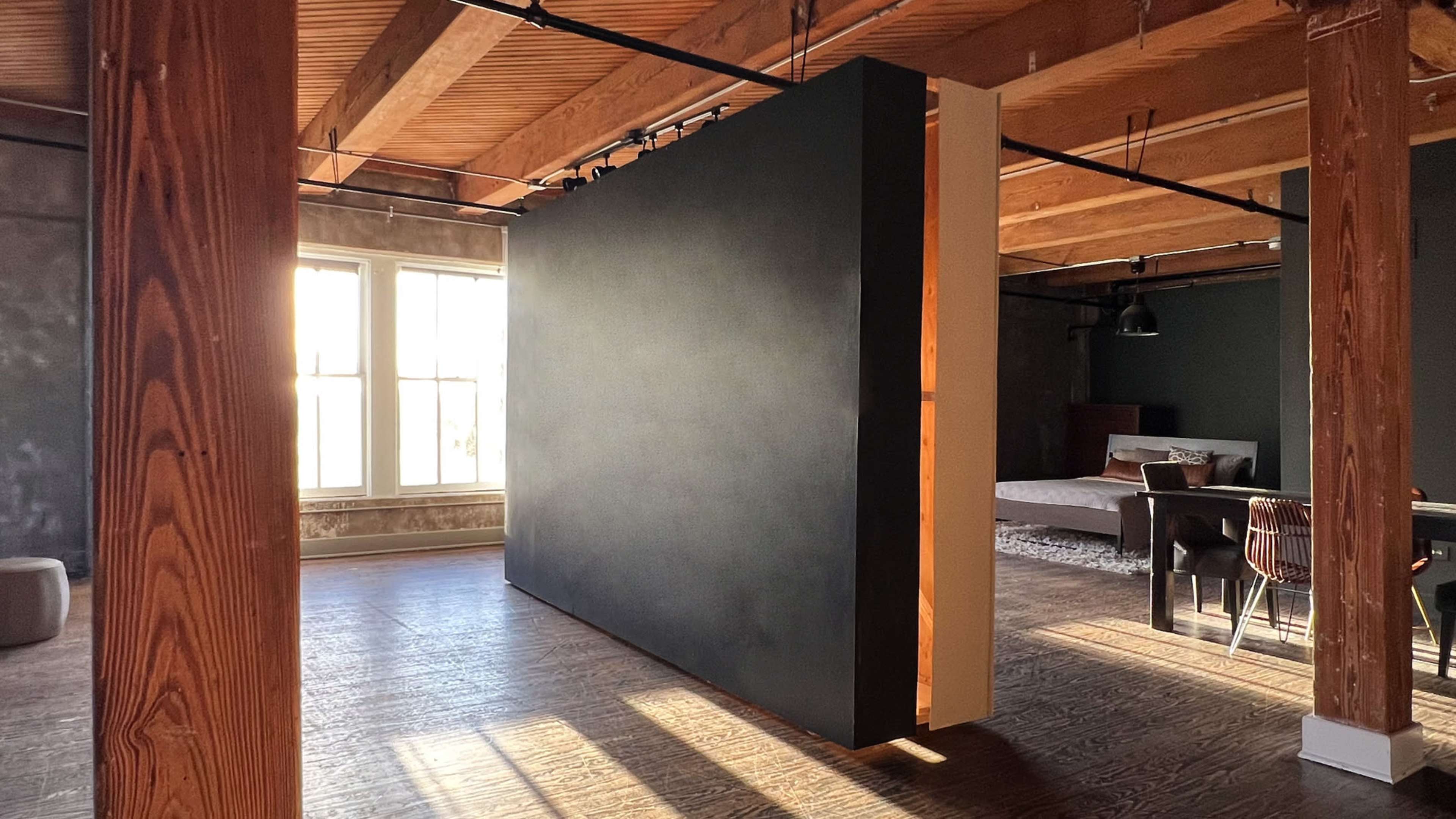 An open-concept interior space with exposed wooden beams, featuring a large black partition separating areas with natural light coming through windows.