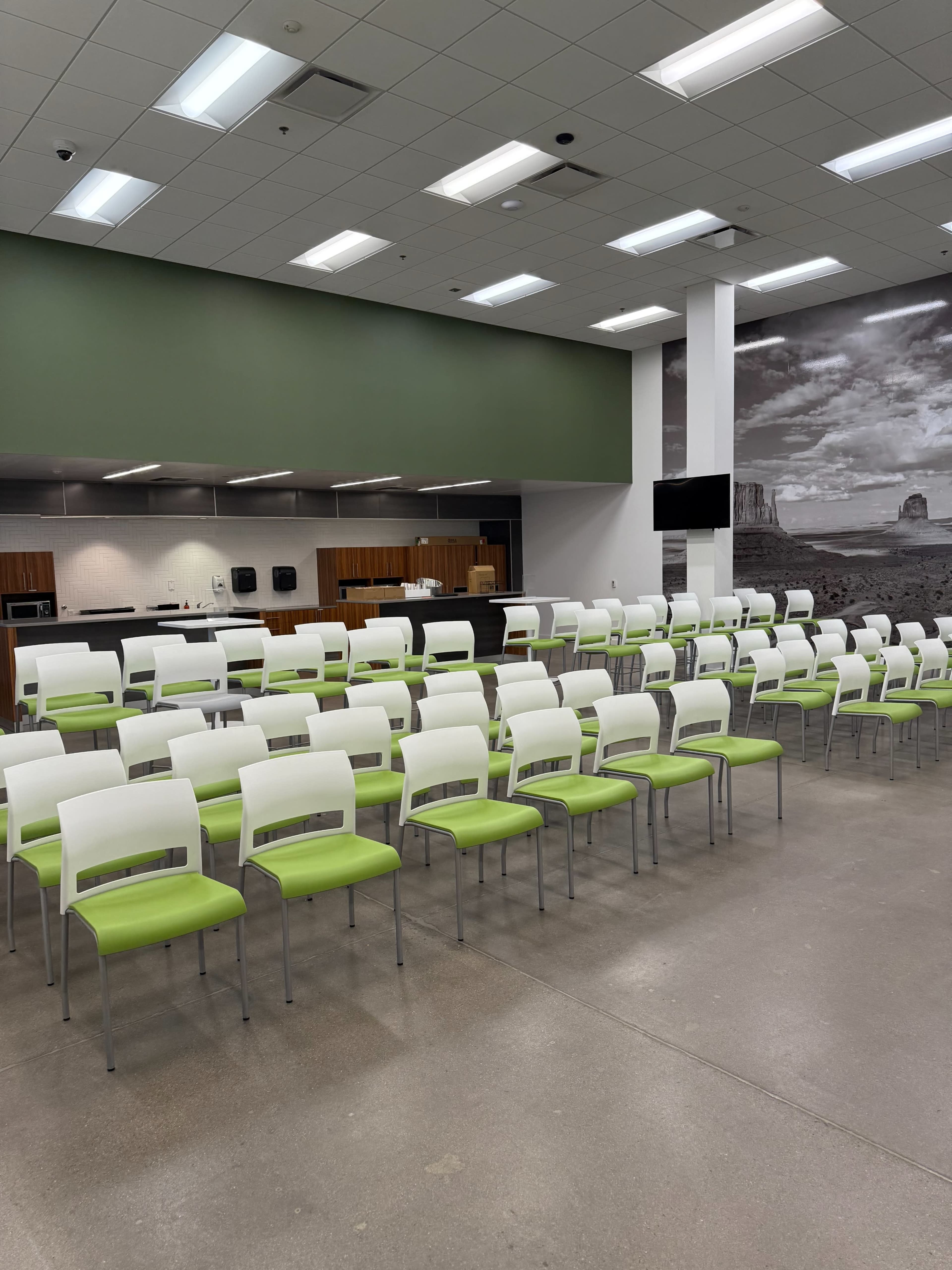 The image shows a row of green and white chairs arranged neatly in a large, modern kitchen or dining area with a service counter in the background.