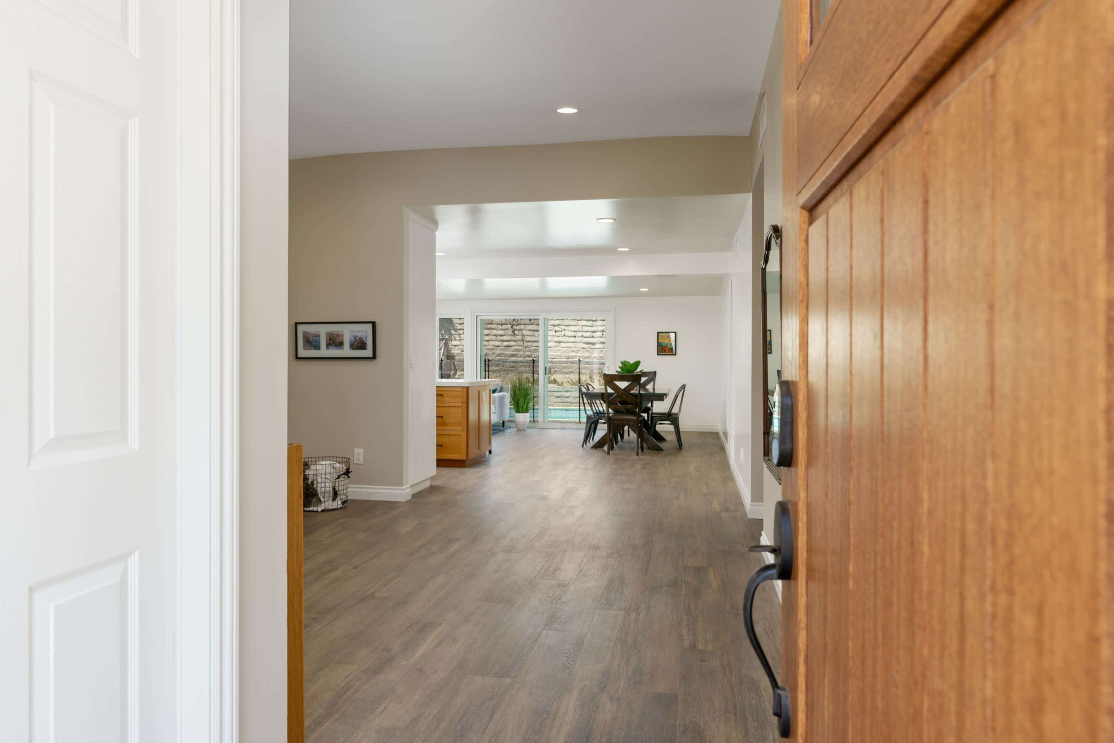 The image shows an open doorway leading into a bright, modern home with a dining area and sliding glass doors at the back.