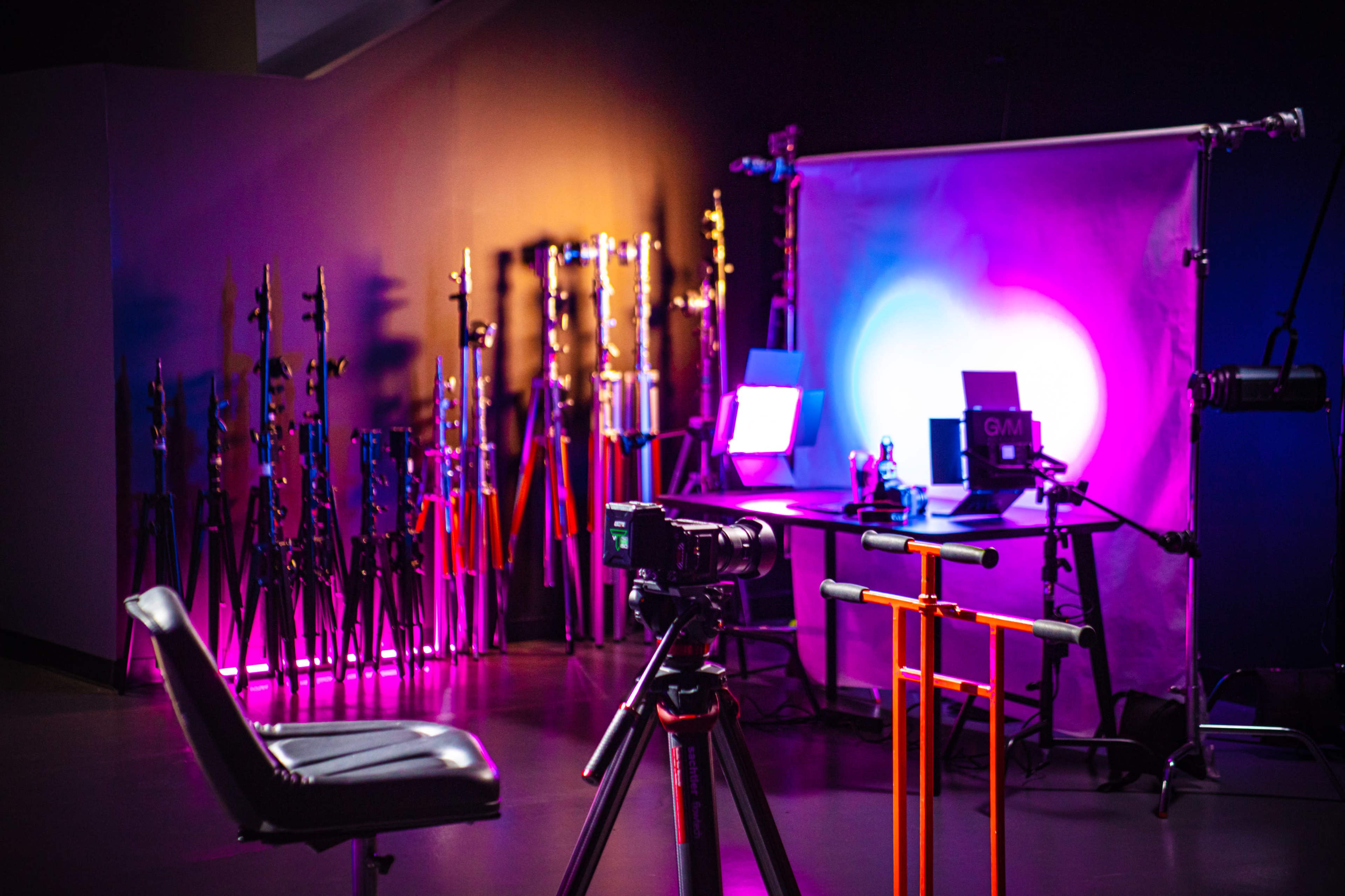 A photography setup features a camera on a tripod facing a brightly lit backdrop, with light stands and equipment arranged in the background.