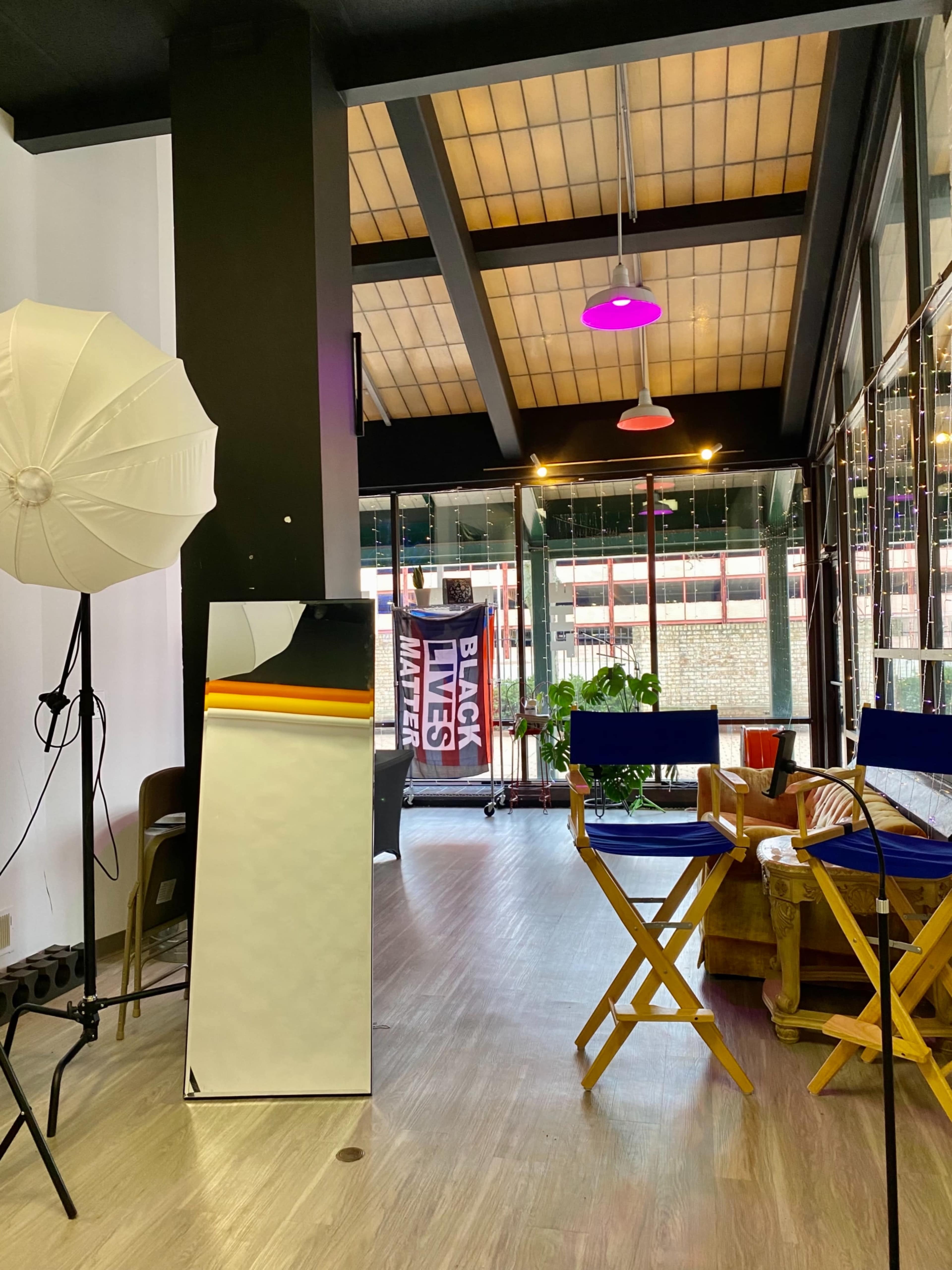The image shows a bright interior space with a large mirror, chairs, a photography light, and a "Black Lives Matter" banner visible through a glass door.