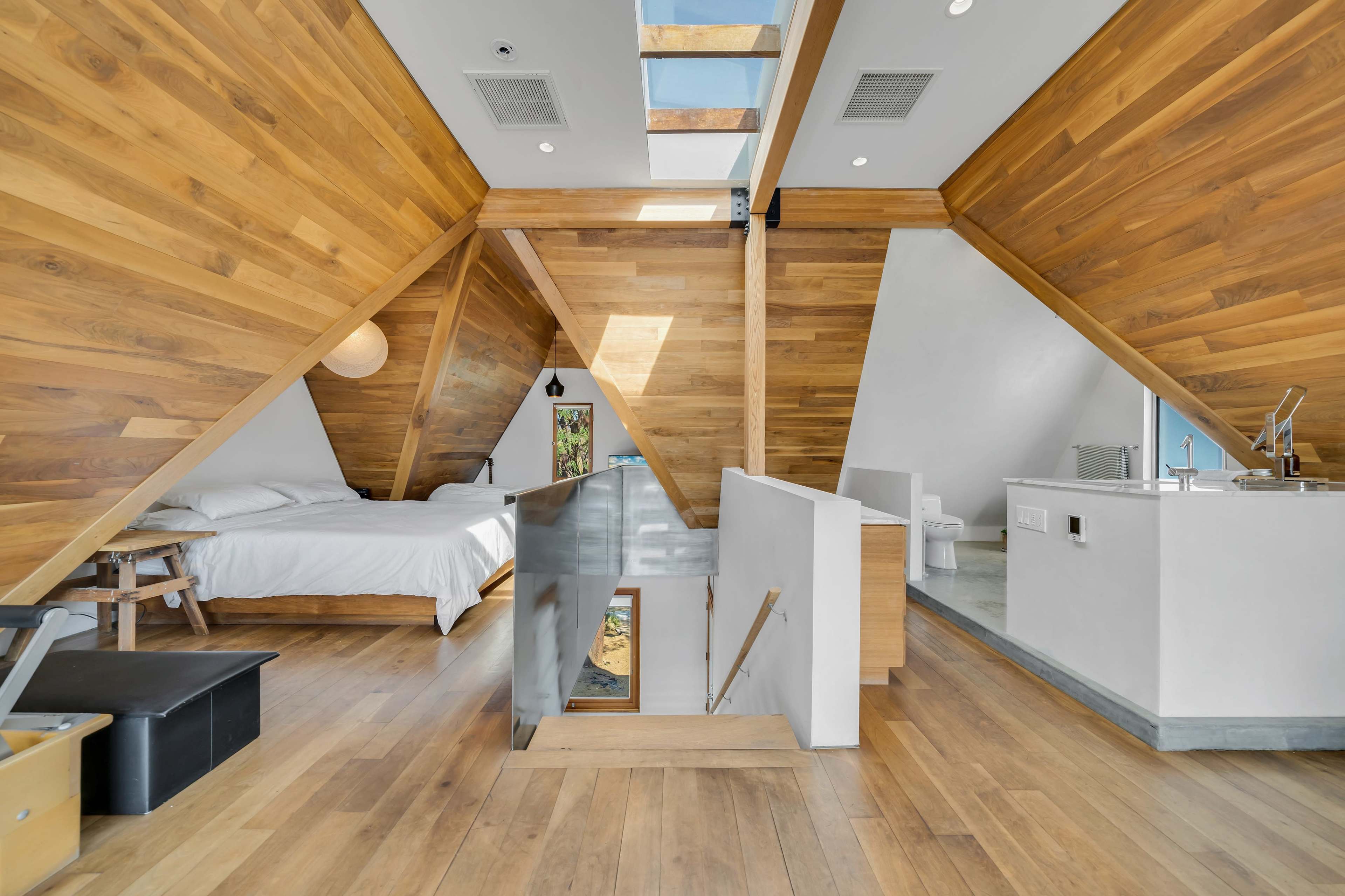 A modern wooden interior features a bedroom with a bed and a kitchenette within a sloped roof structure.