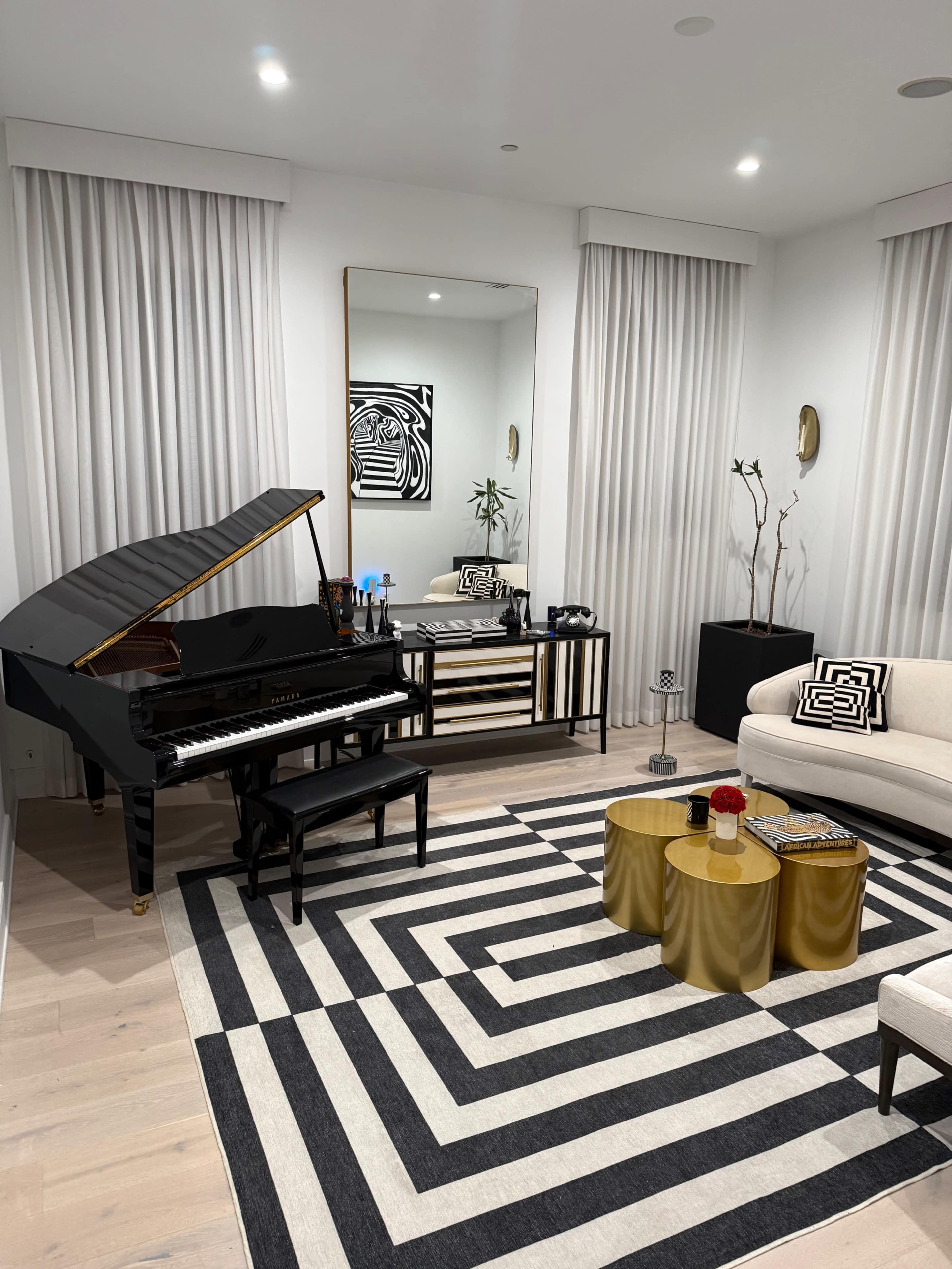 The image shows a modern living room featuring a black grand piano, a striped area rug, and a light-colored sofa, with decorative elements including a mirror and small tables.