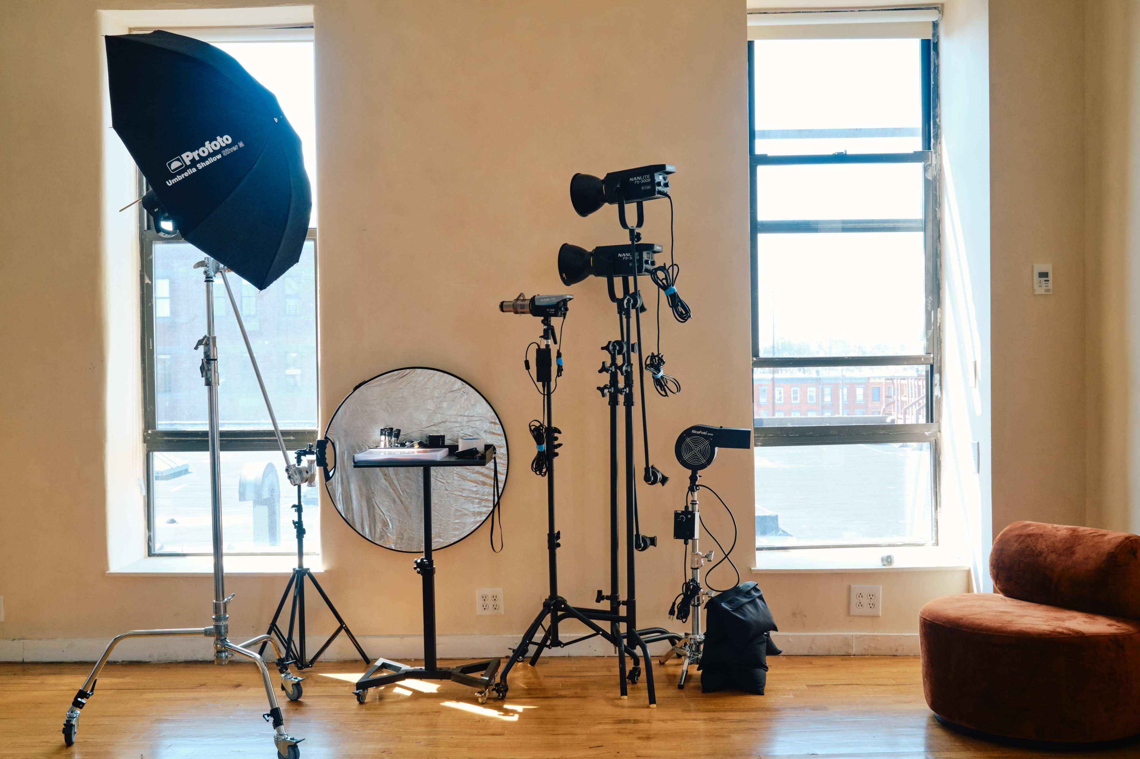 The image shows a photography setup in a well-lit room, featuring various lighting equipment and a circular reflector beside a brown couch.