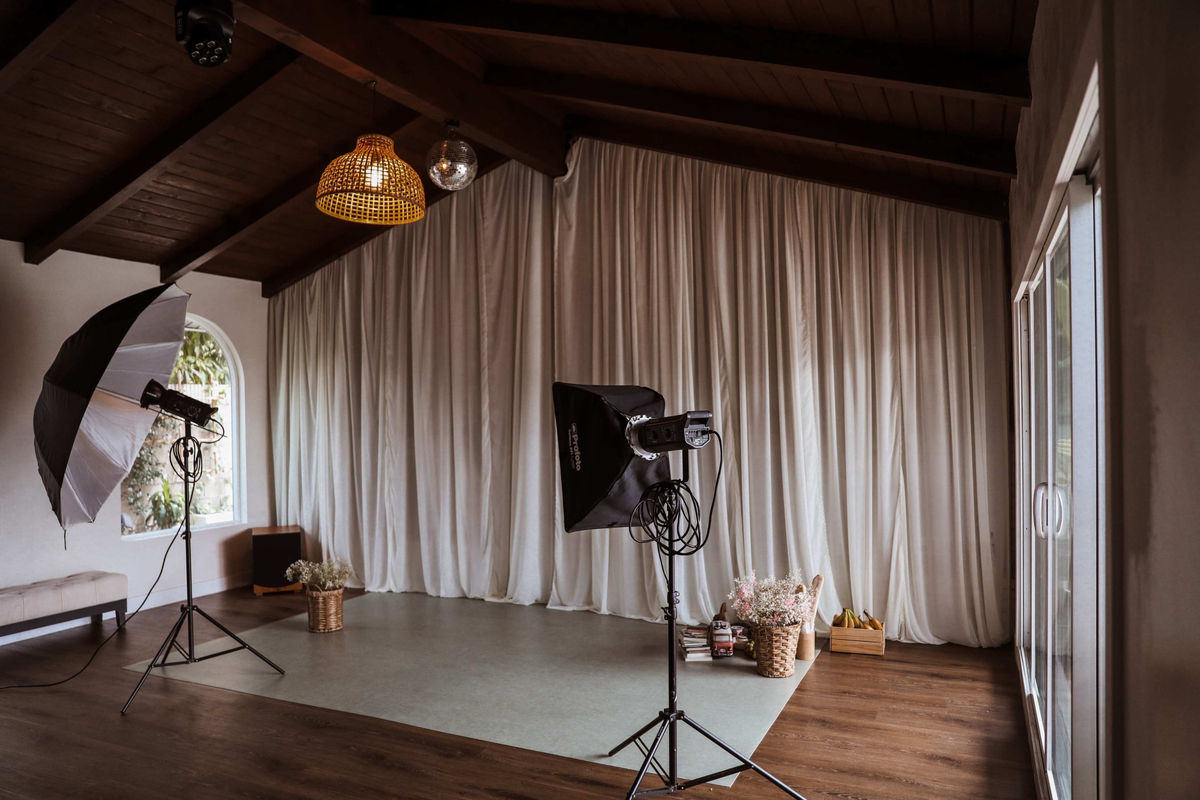 The image shows a spacious indoor area with large light modifiers set up on stands and a backdrop of white curtains along one wall.