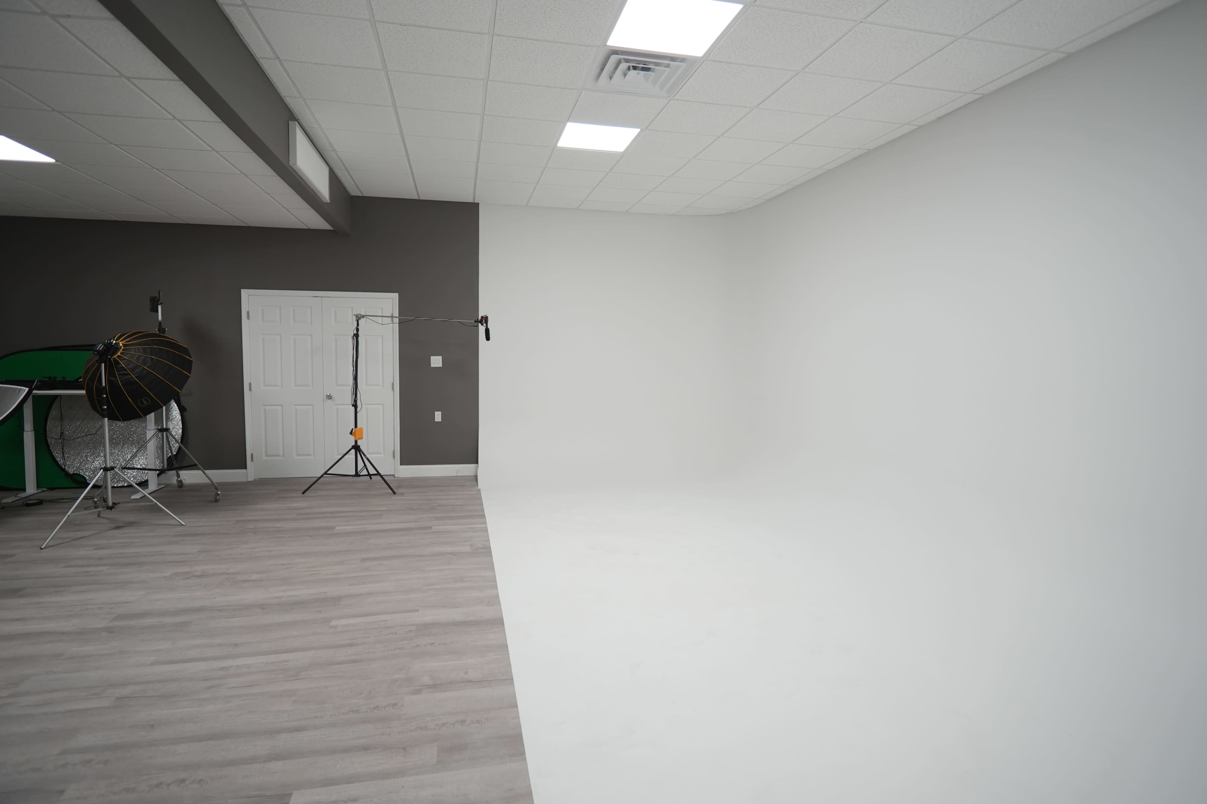 A minimalistic photo studio with a gray wall, white floor, and lighting equipment set up in one corner.