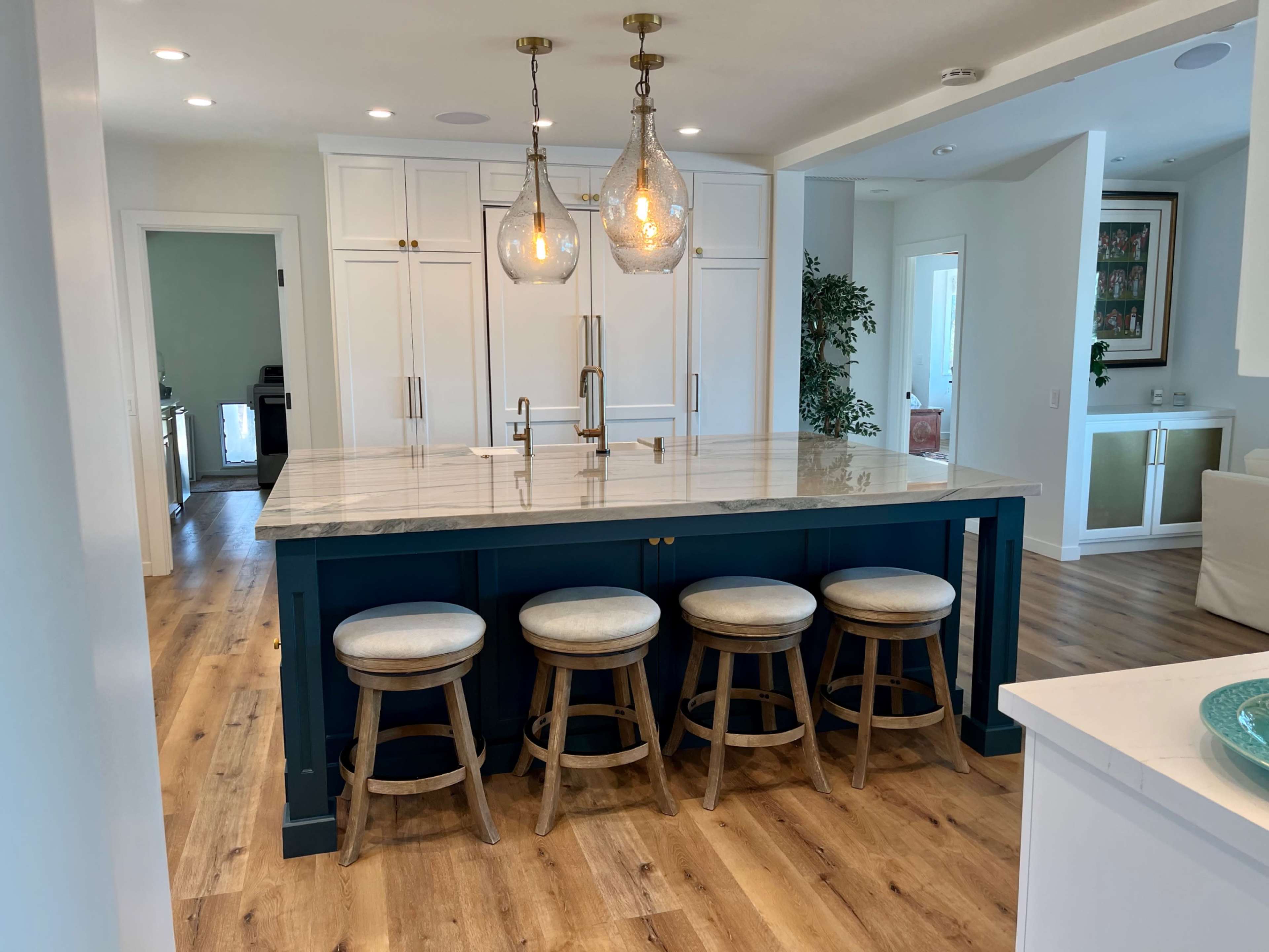 A kitchen features a large marble island with four wooden stools and hanging pendant lights above.