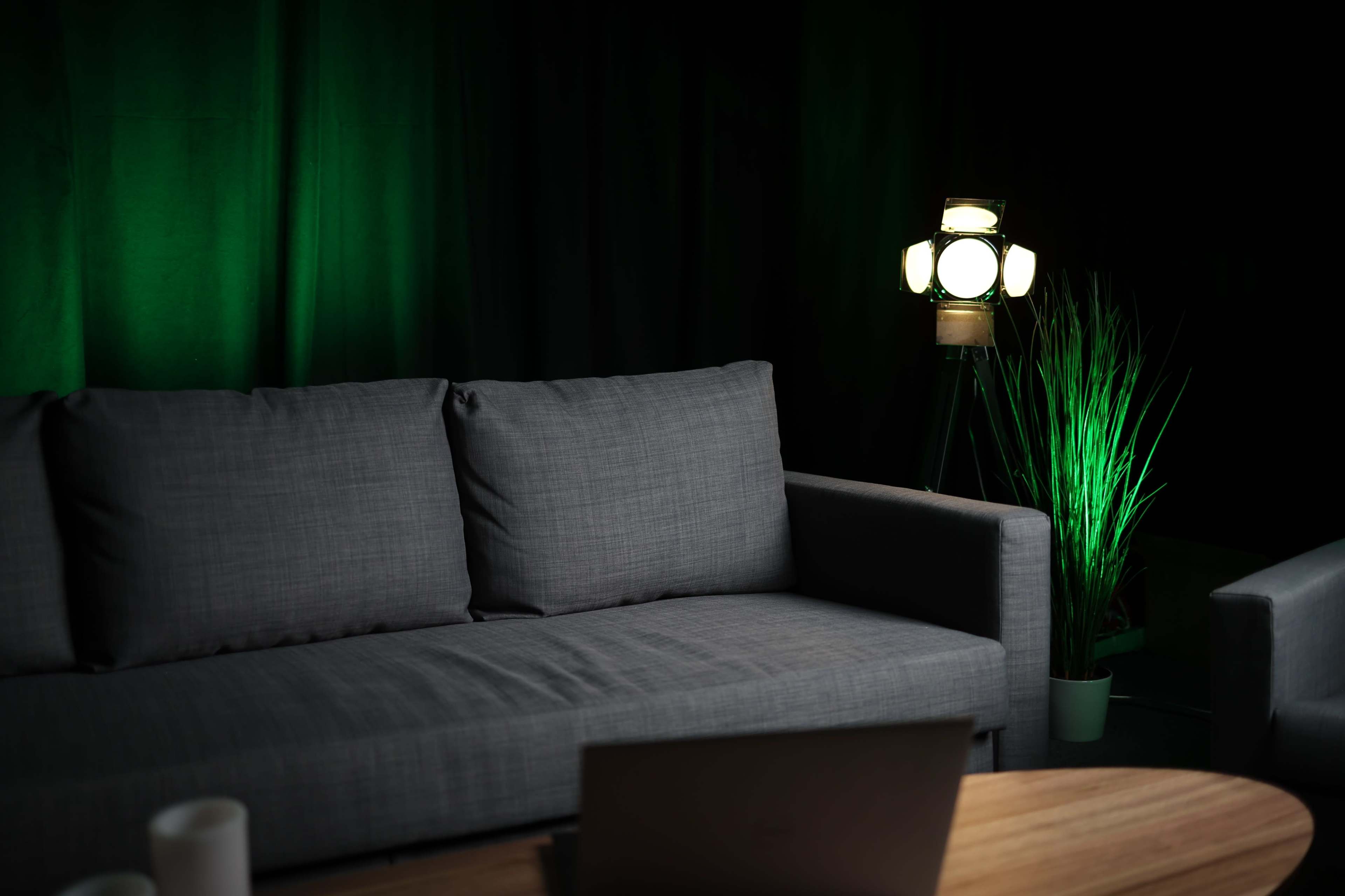 A gray couch is positioned in a dimly lit room with green background lighting and a floor lamp.