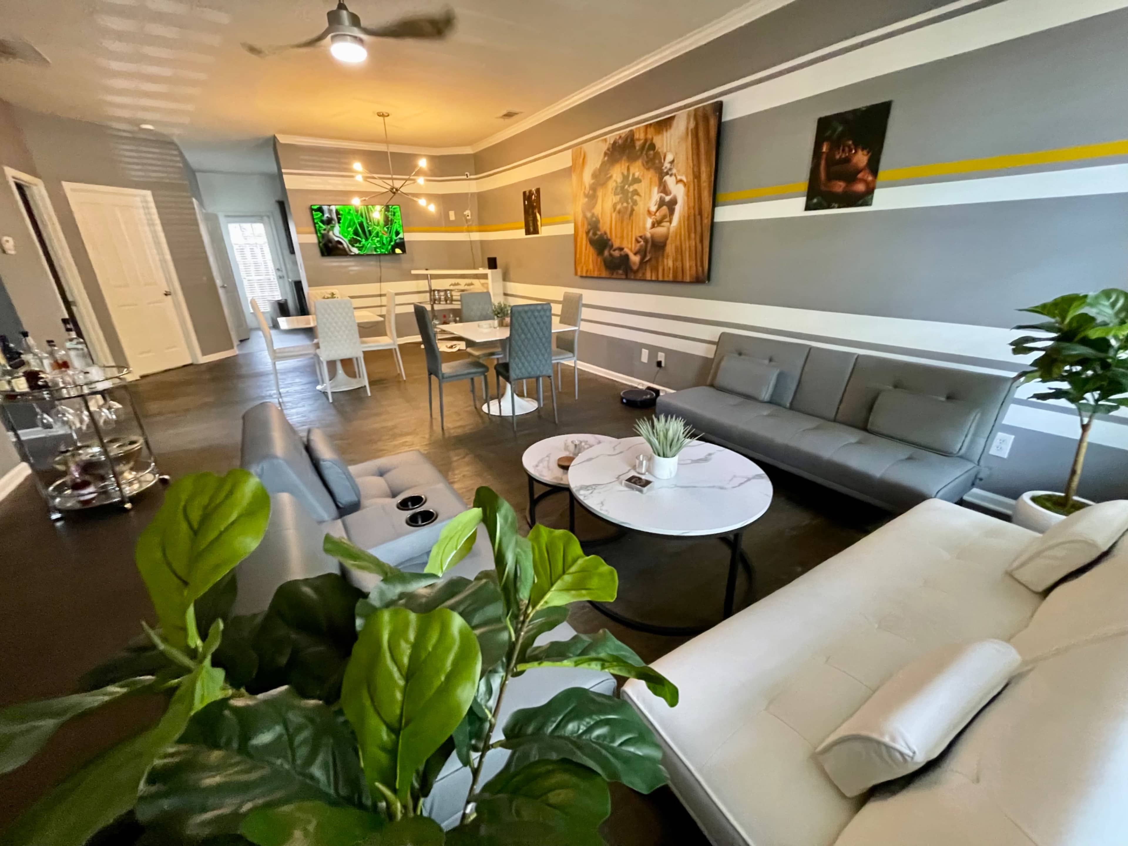 A modern living room with gray walls, a large television mounted on the wall, a circular coffee table, and a mix of seating arrangements including gray sofas and dining chairs.