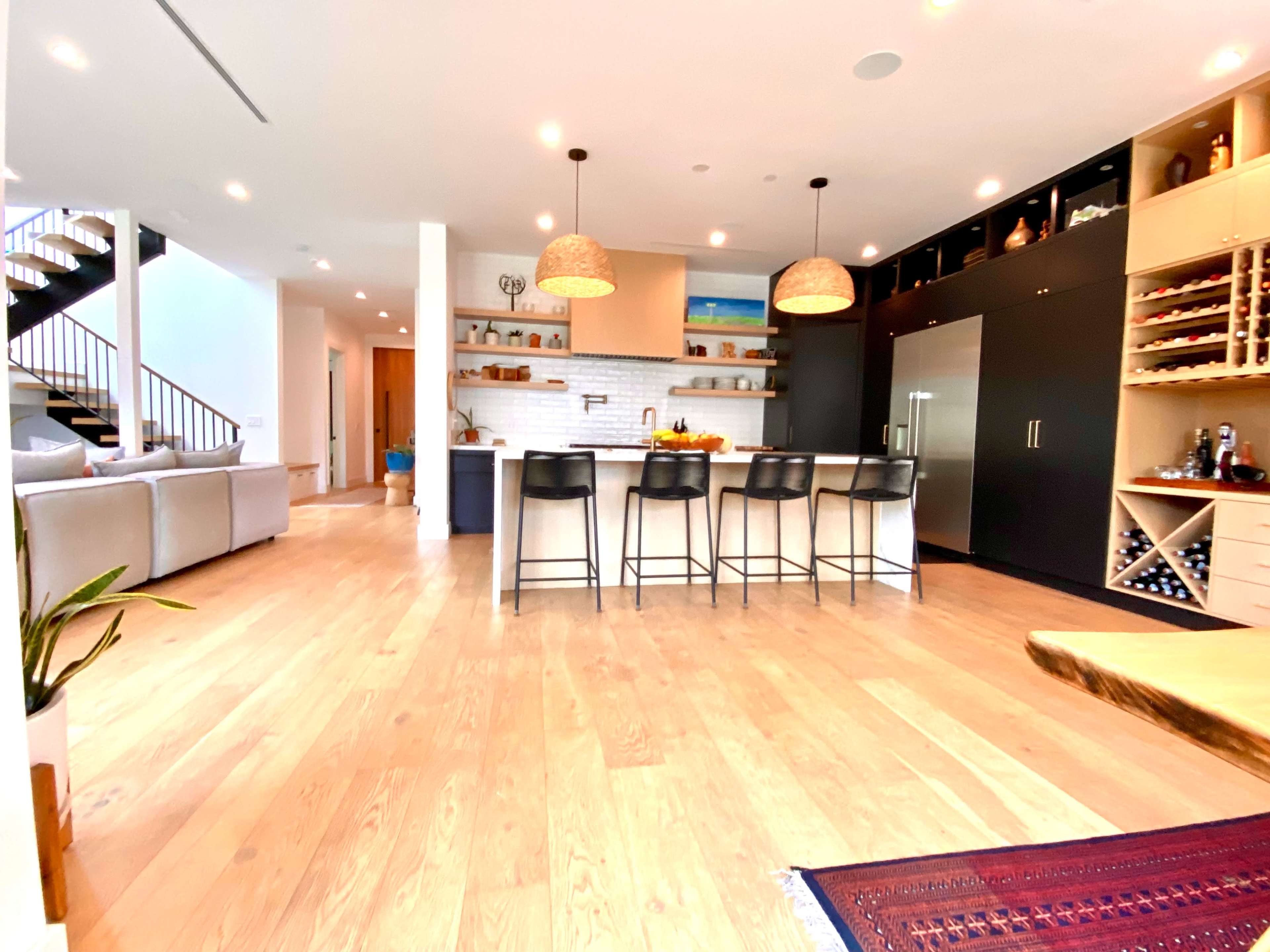 A modern kitchen and living area featuring a large island with bar stools, a staircase in the background, and ample cabinetry.