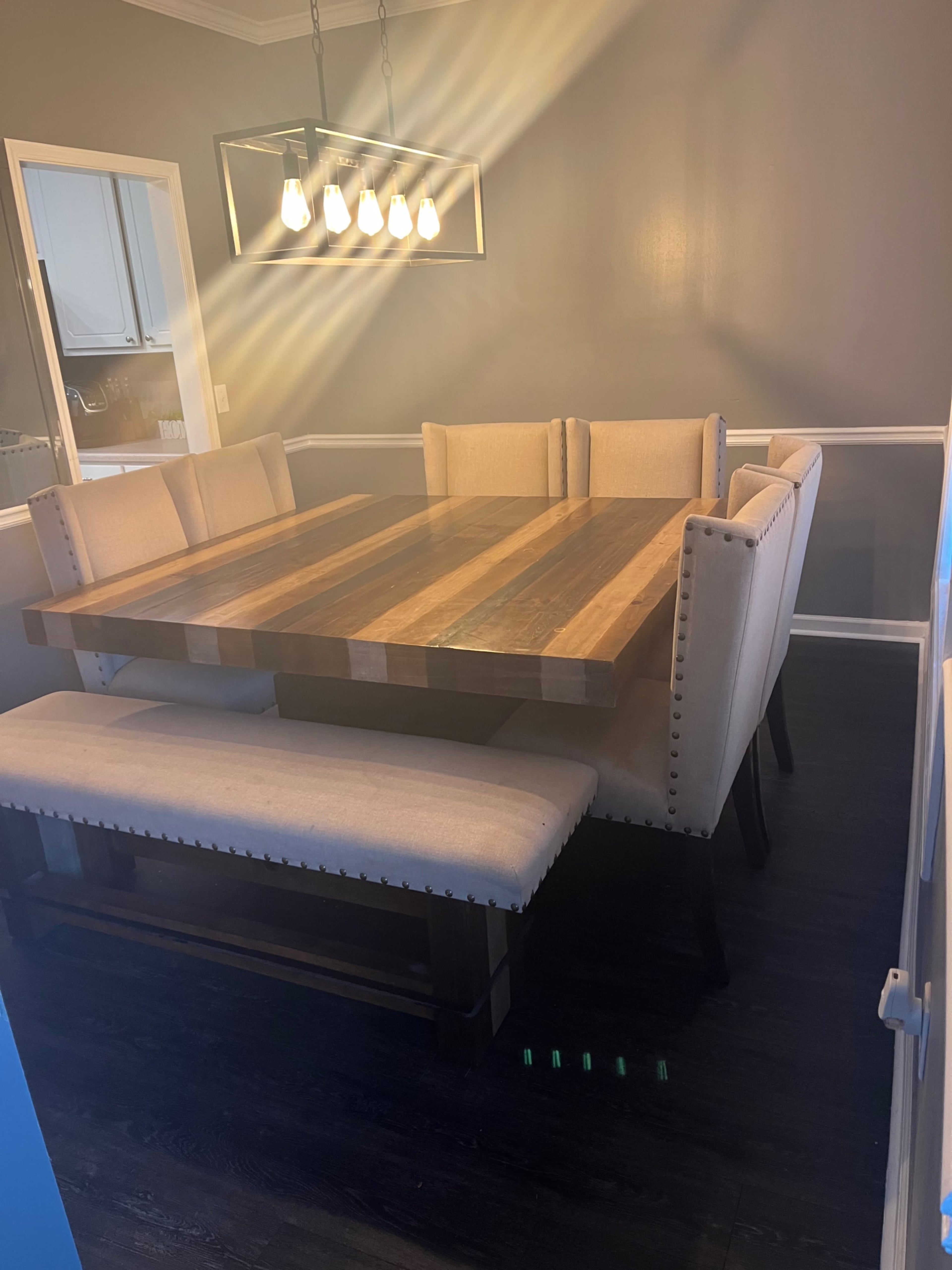 A wooden dining table with a striped design is surrounded by upholstered chairs and a bench in a well-lit dining room.