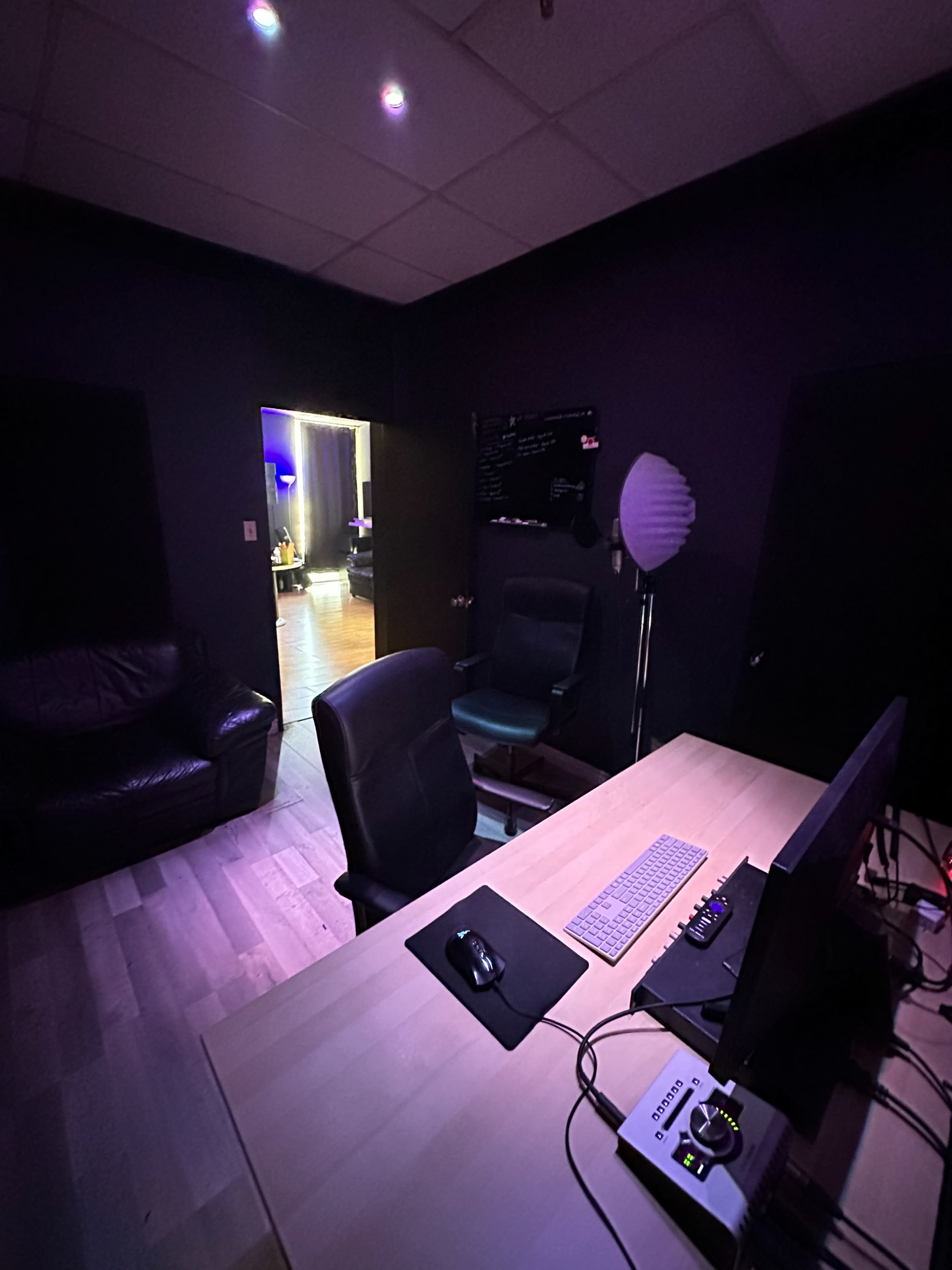 The image shows a dimly lit office space with a large desk, two office chairs, a couch, and an open doorway leading to another room.