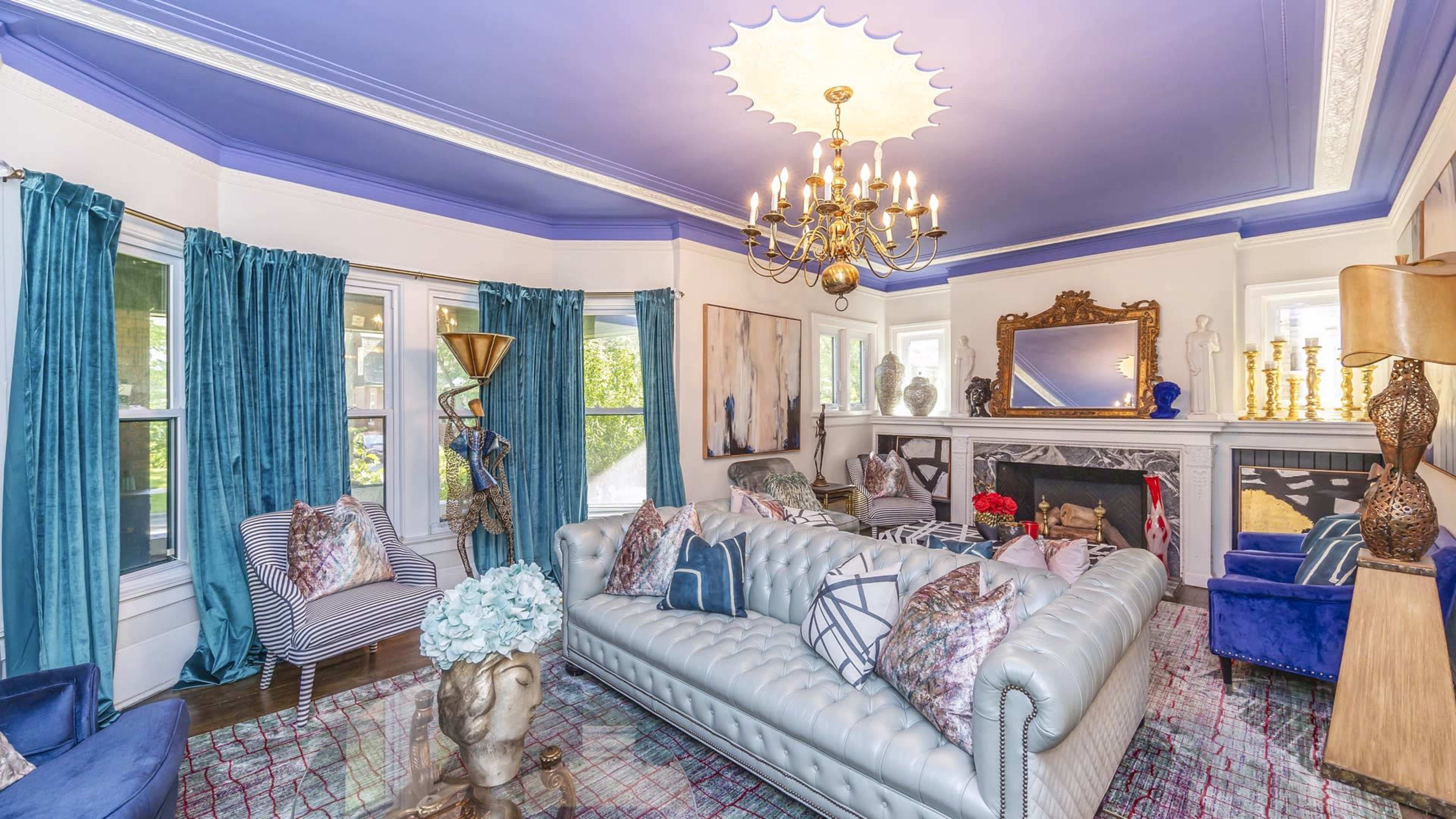 The living room features a blue ceiling, a chandelier, a light-colored sofa with decorative cushions, and various pieces of artwork and decor.