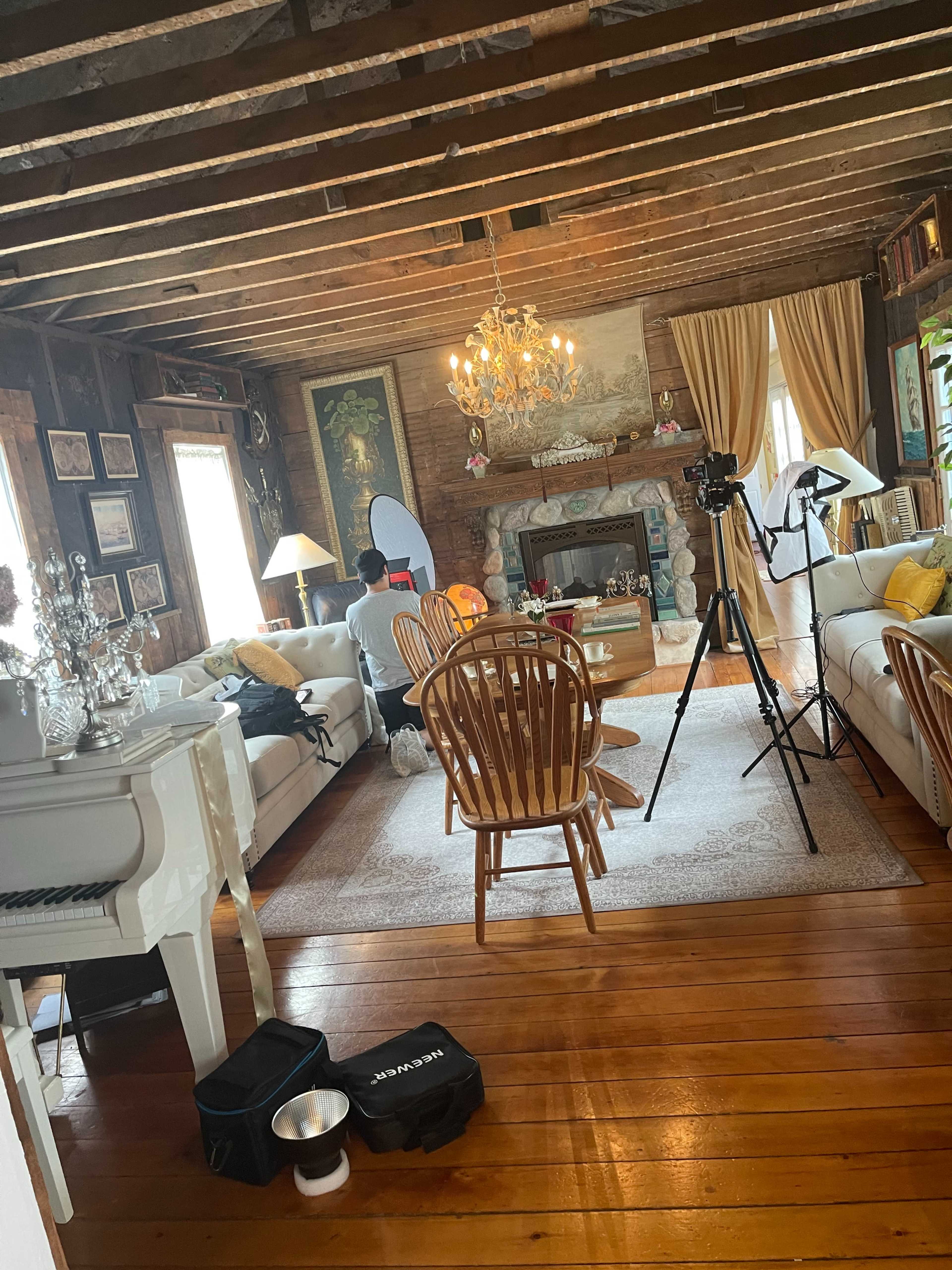 A rustic living room with wooden beams, two sofas, a coffee table, and a chandelier, along with photography equipment set up in one corner.