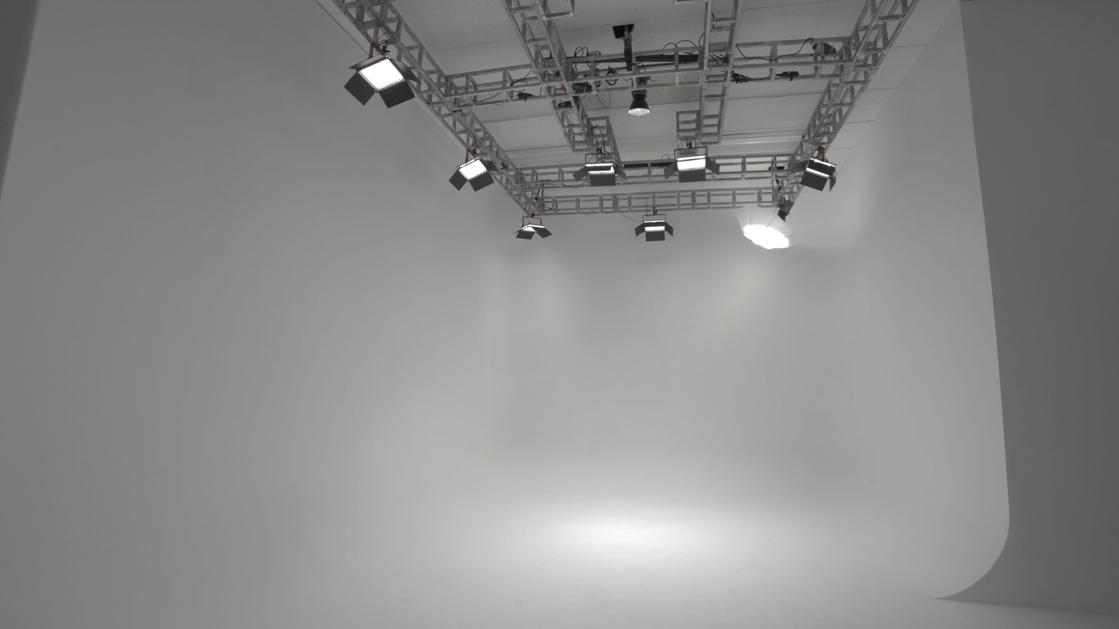 A minimalist studio space with a blank white backdrop and overhead lighting fixtures.