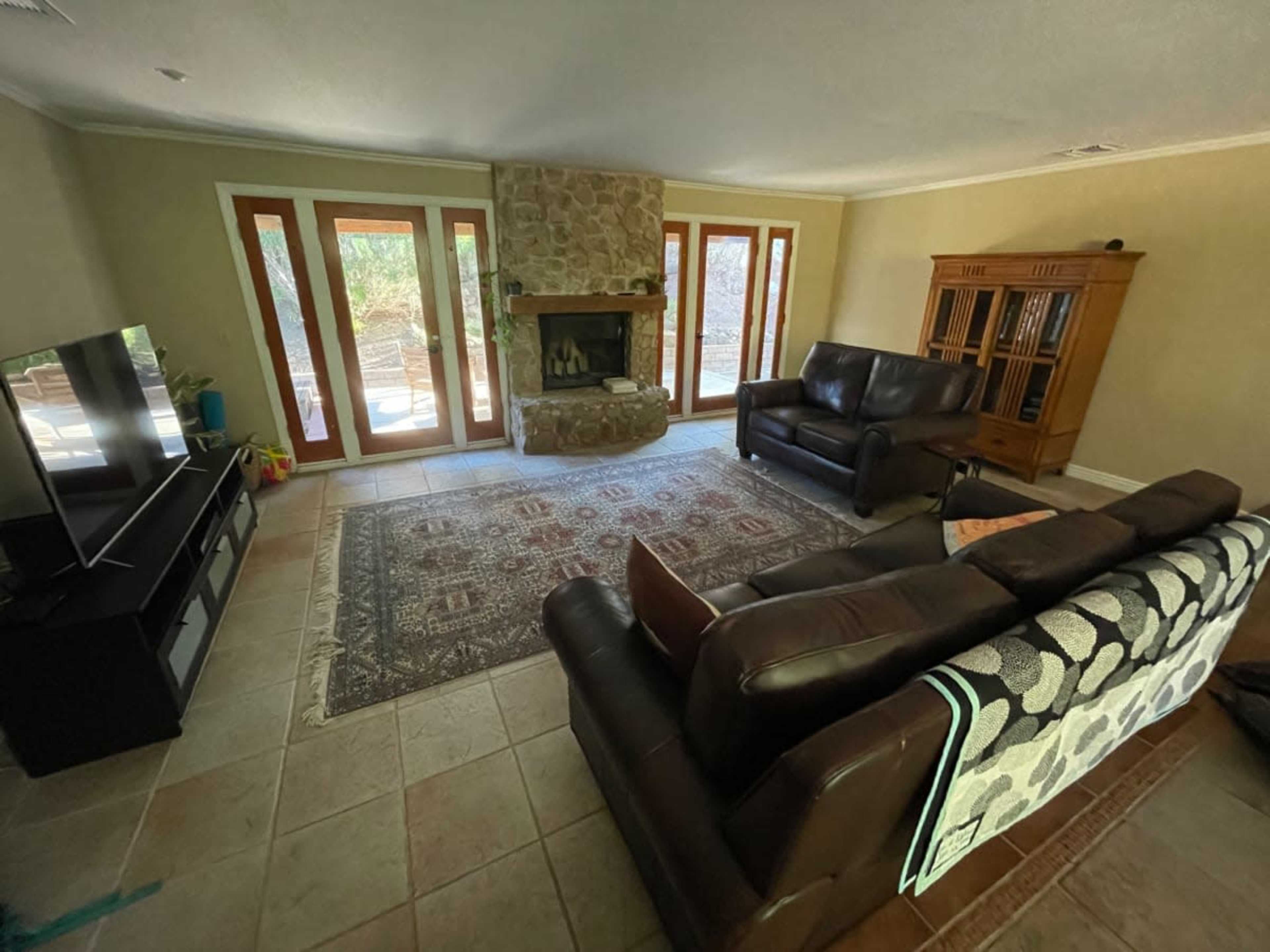A living room features a stone fireplace, two leather sofas, a television, and large glass doors leading to an outdoor area.
