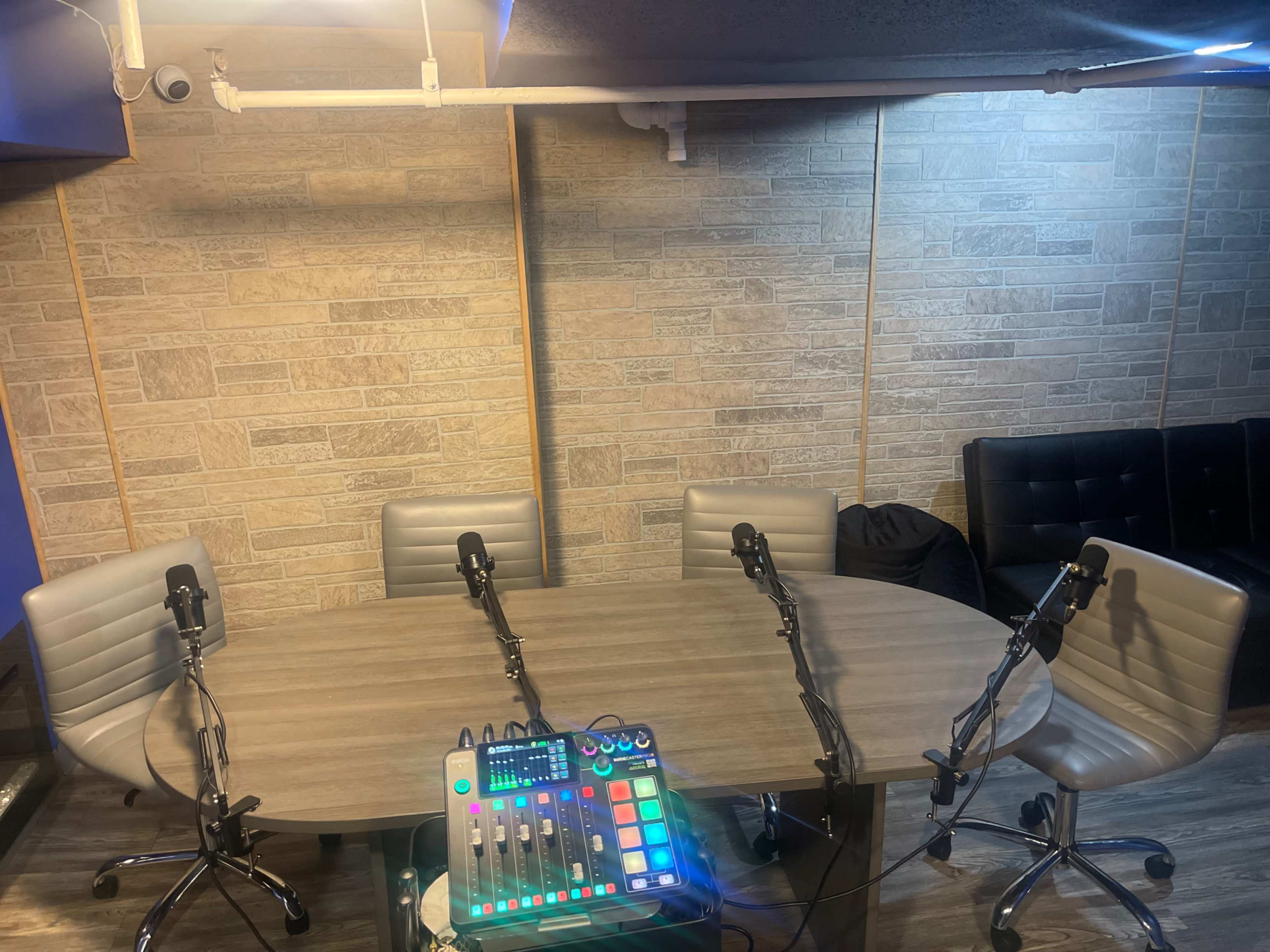 A microphone-equipped round table surrounded by four chairs, with audio equipment positioned in the center and a textured stone wall in the background.
