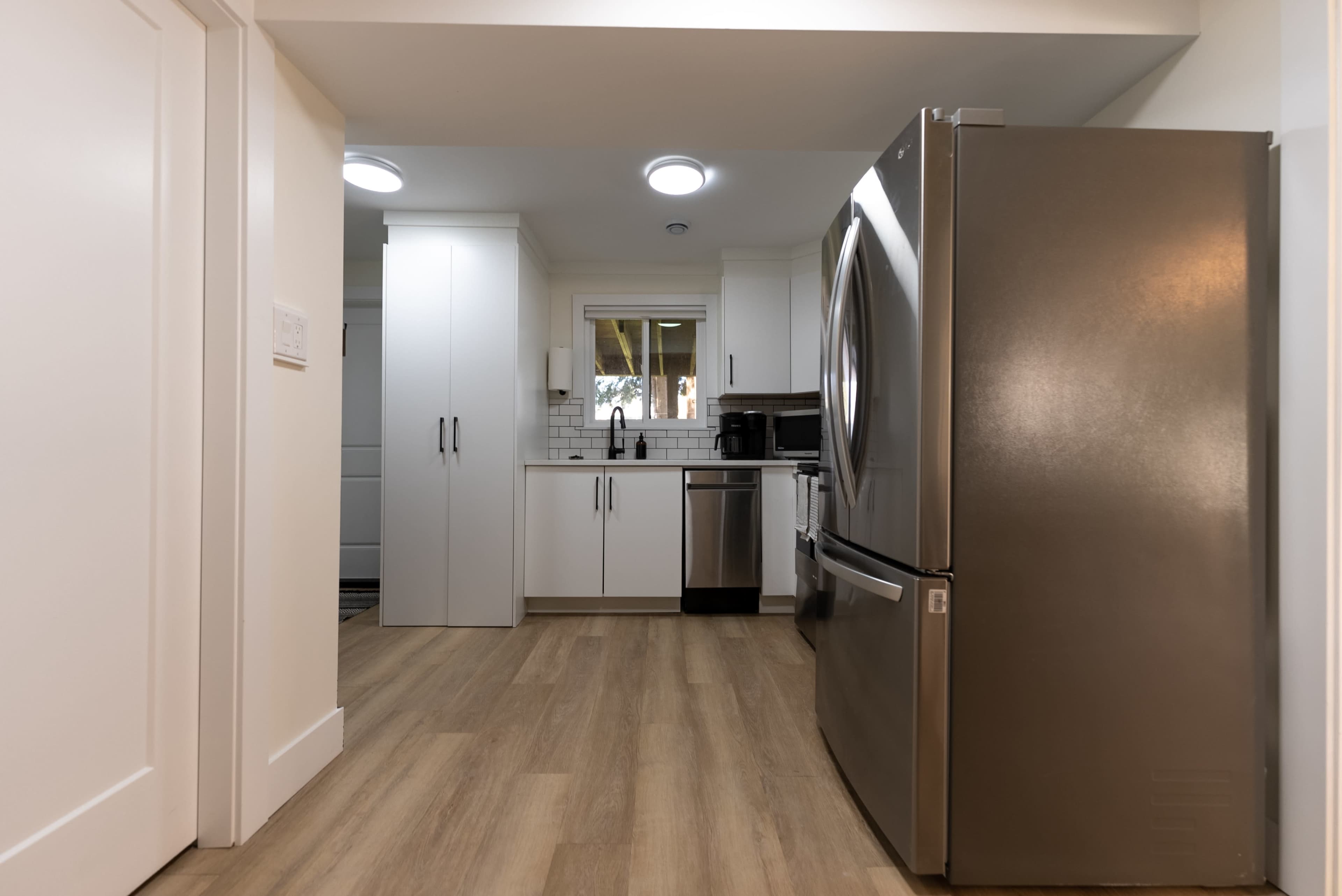 A modern kitchen featuring a stainless steel refrigerator, white cabinets, and light hardwood flooring.