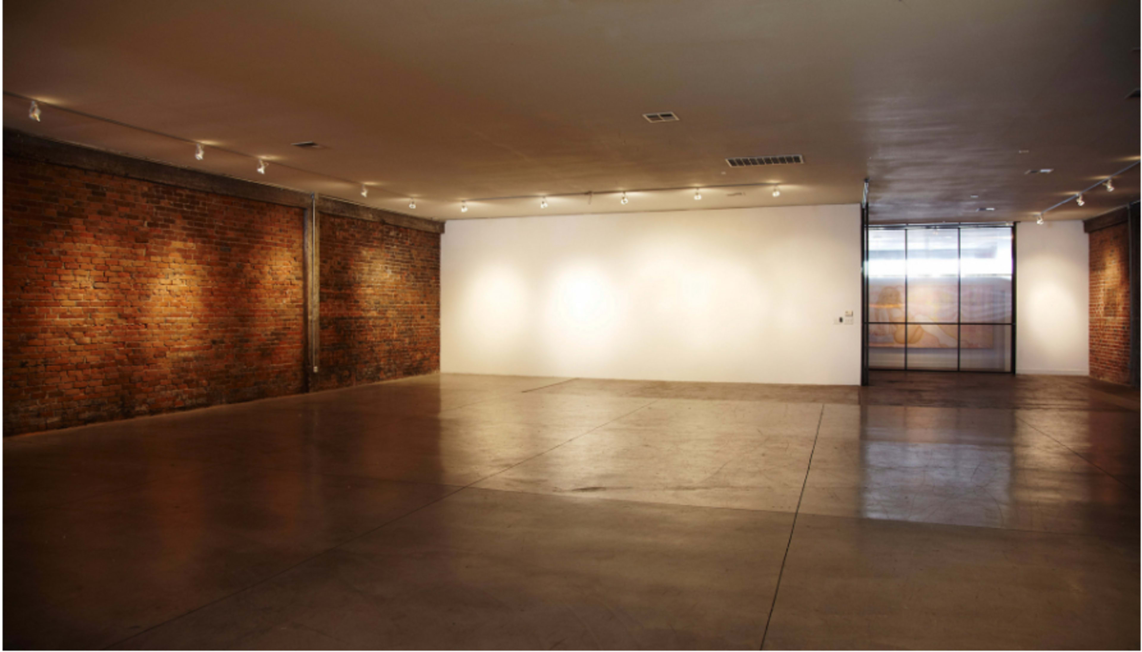 An empty art gallery features exposed brick walls and concrete flooring under soft overhead lighting.