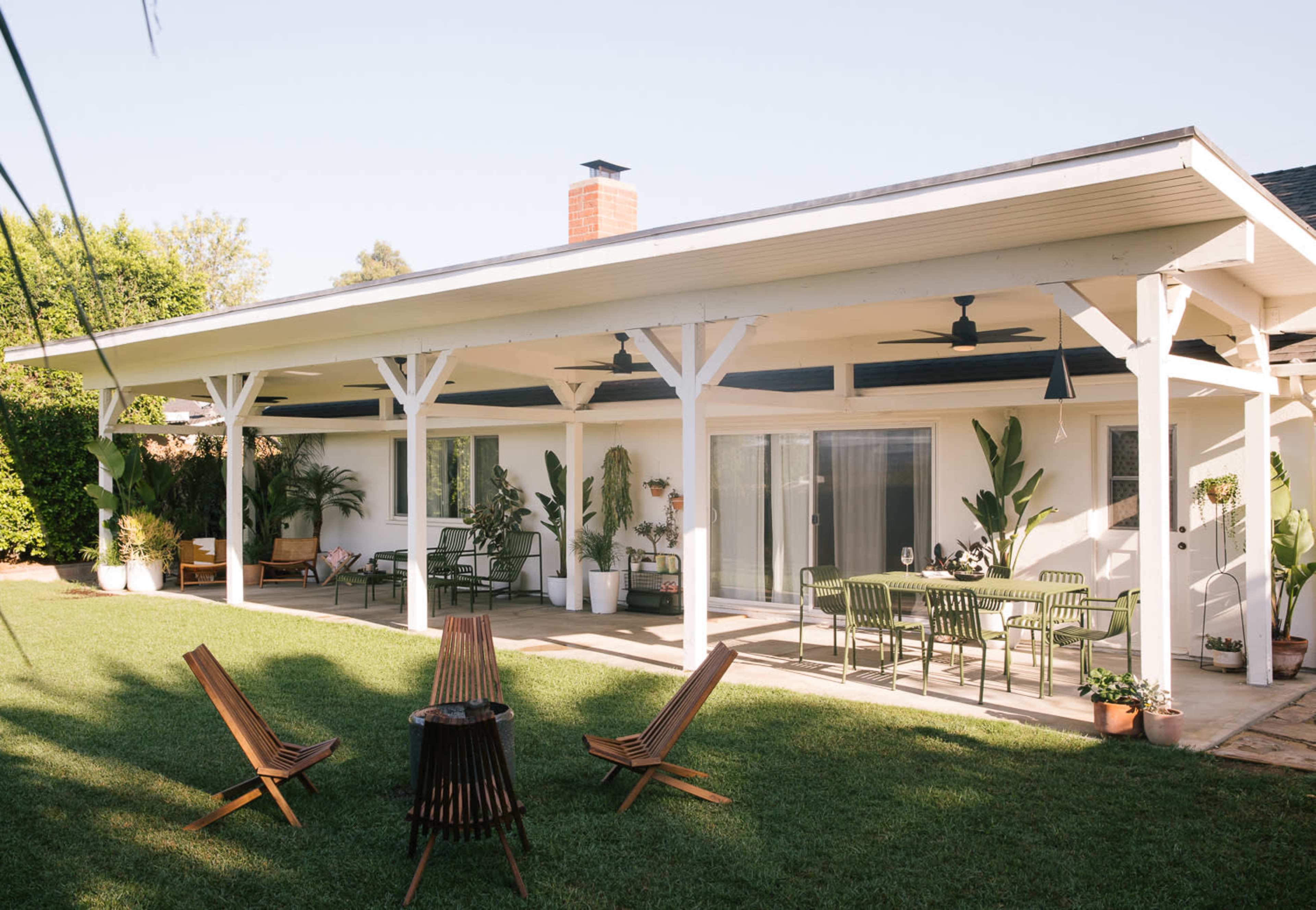 A spacious backyard features a covered patio with seating and a dining area surrounded by potted plants and a well-maintained lawn.