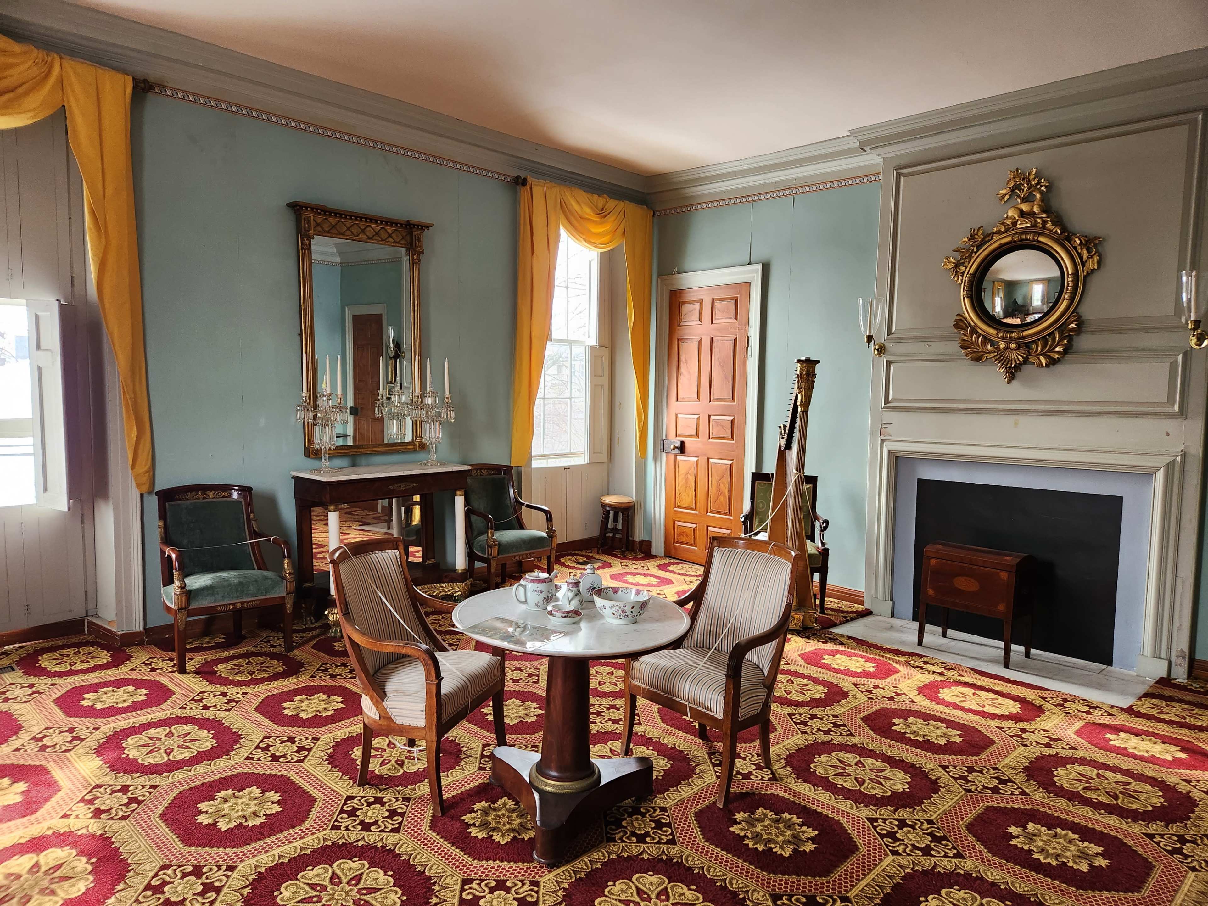 A furnished interior of a room with a table and chairs, a fireplace, and decorative elements like a mirror and curtains.