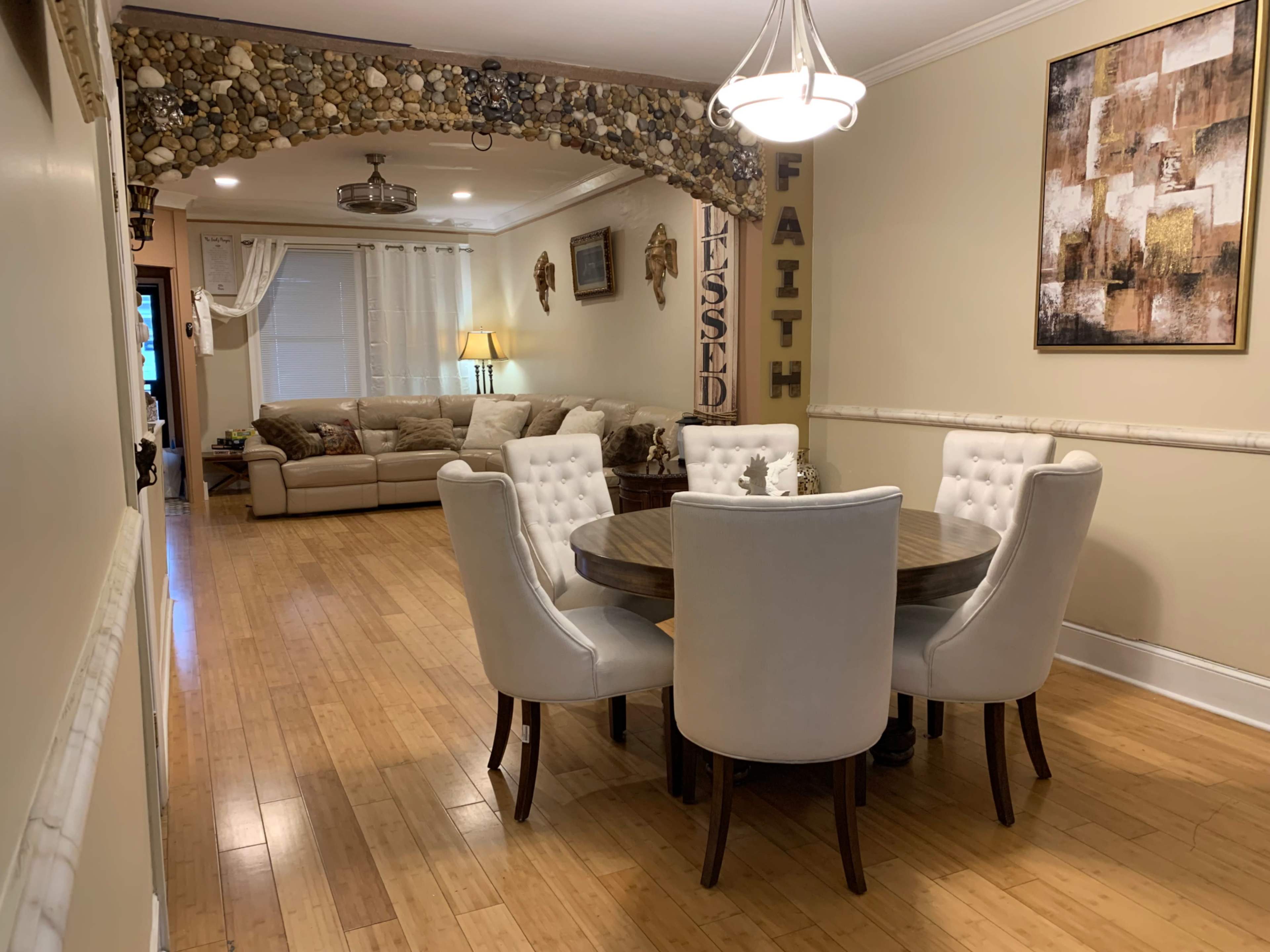 A dining area features a round table surrounded by white upholstered chairs, with a cozy living room visible in the background.