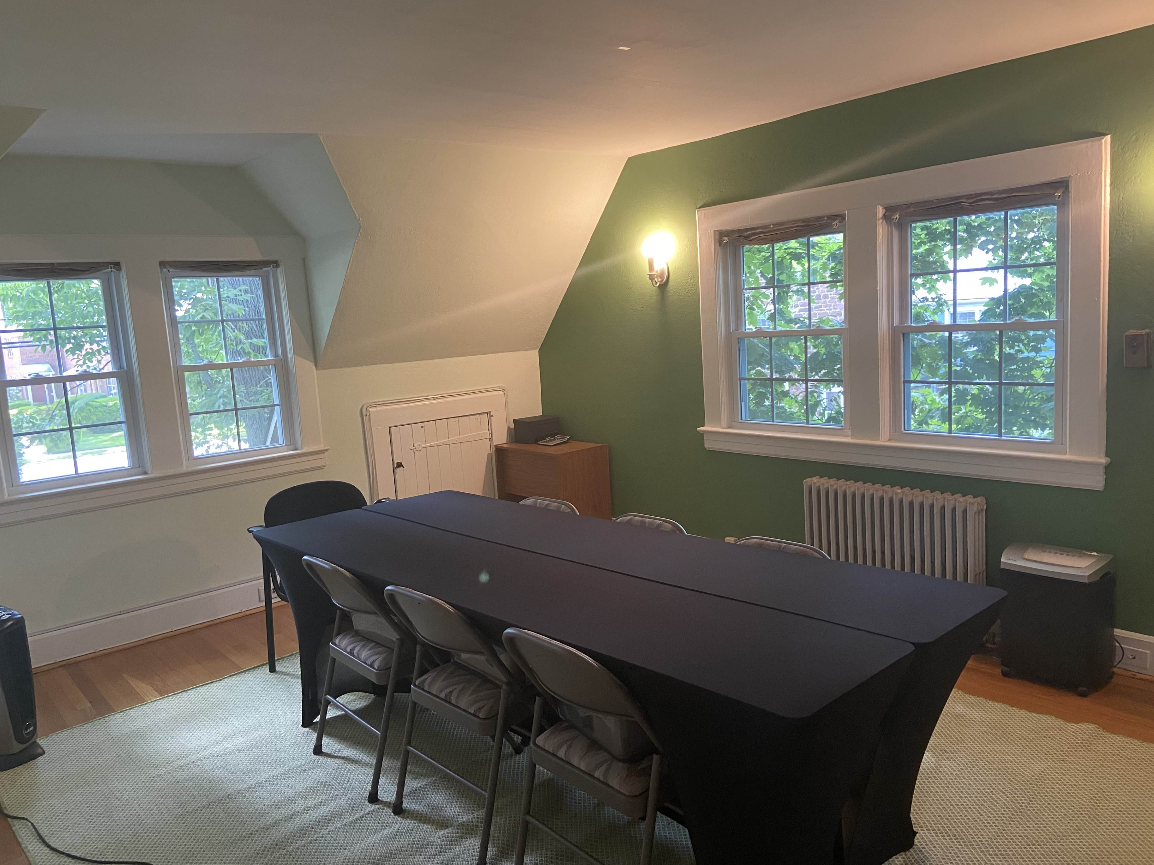A conference room with a long table set for meetings, surrounded by chairs, and large windows allowing natural light to enter.