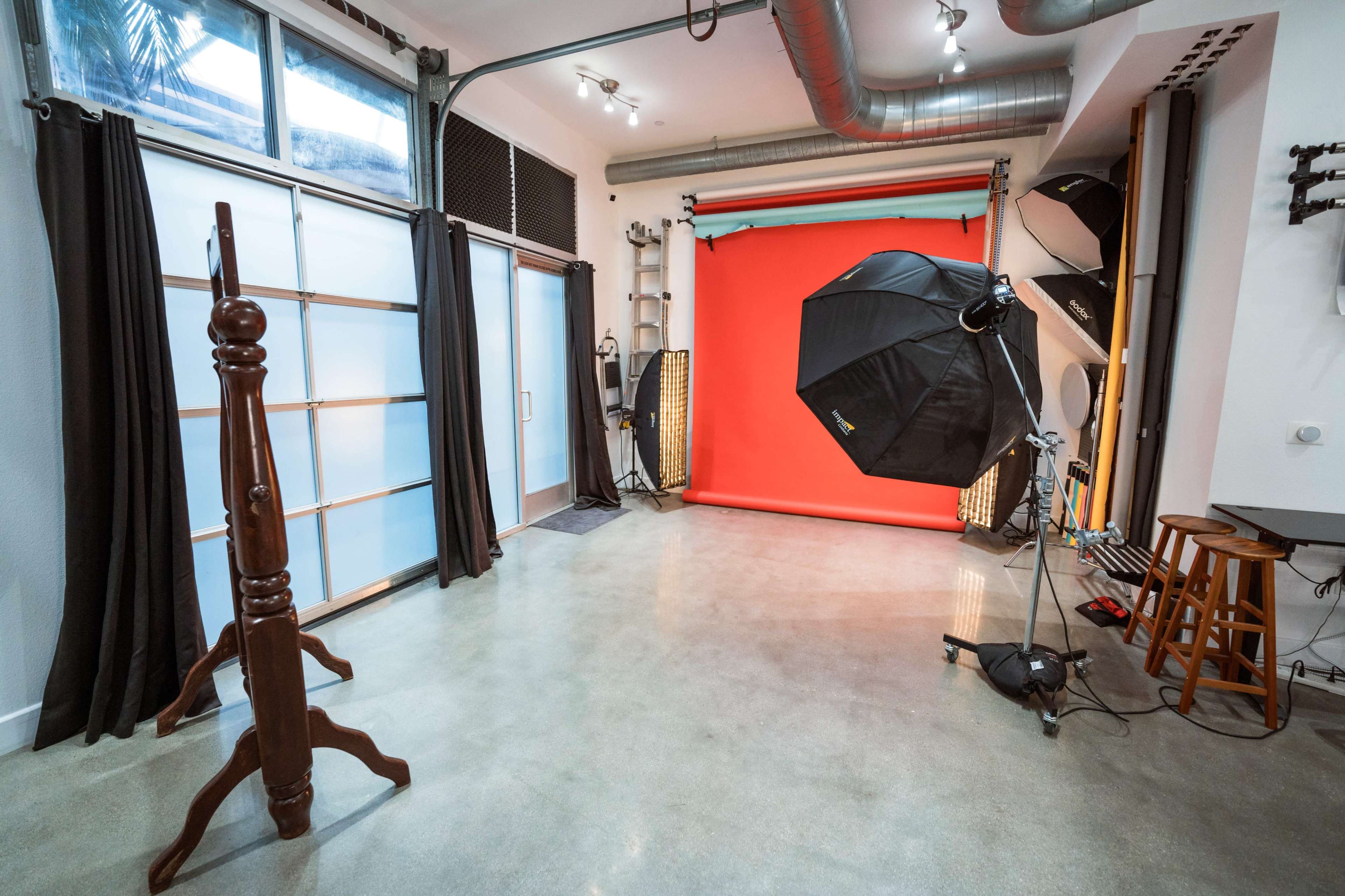 A photography studio with a bright red backdrop, an umbrella light setup, and various equipment arranged in a modern space.