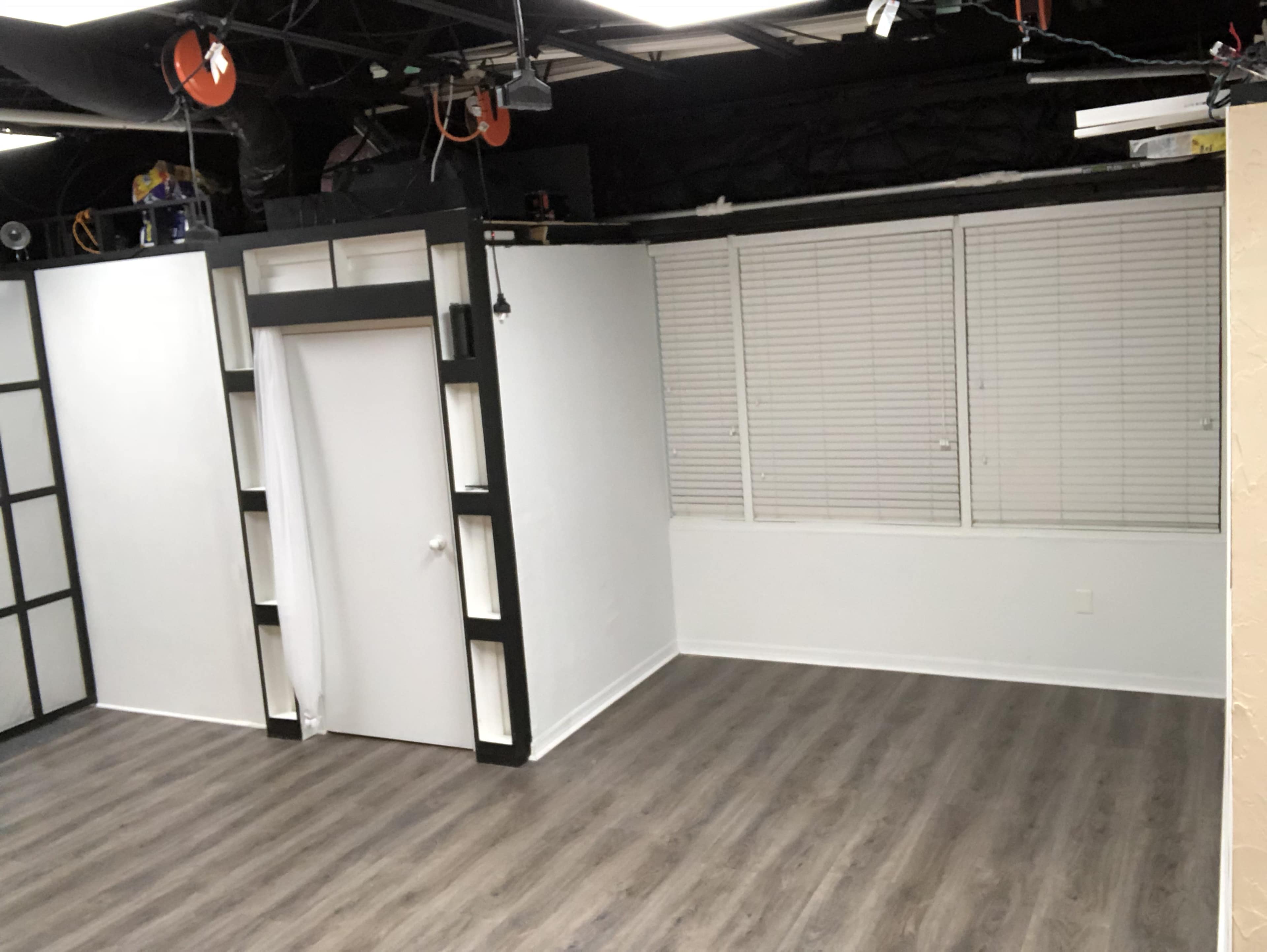 A sparsely furnished room with white walls, a closed door, and wooden flooring.