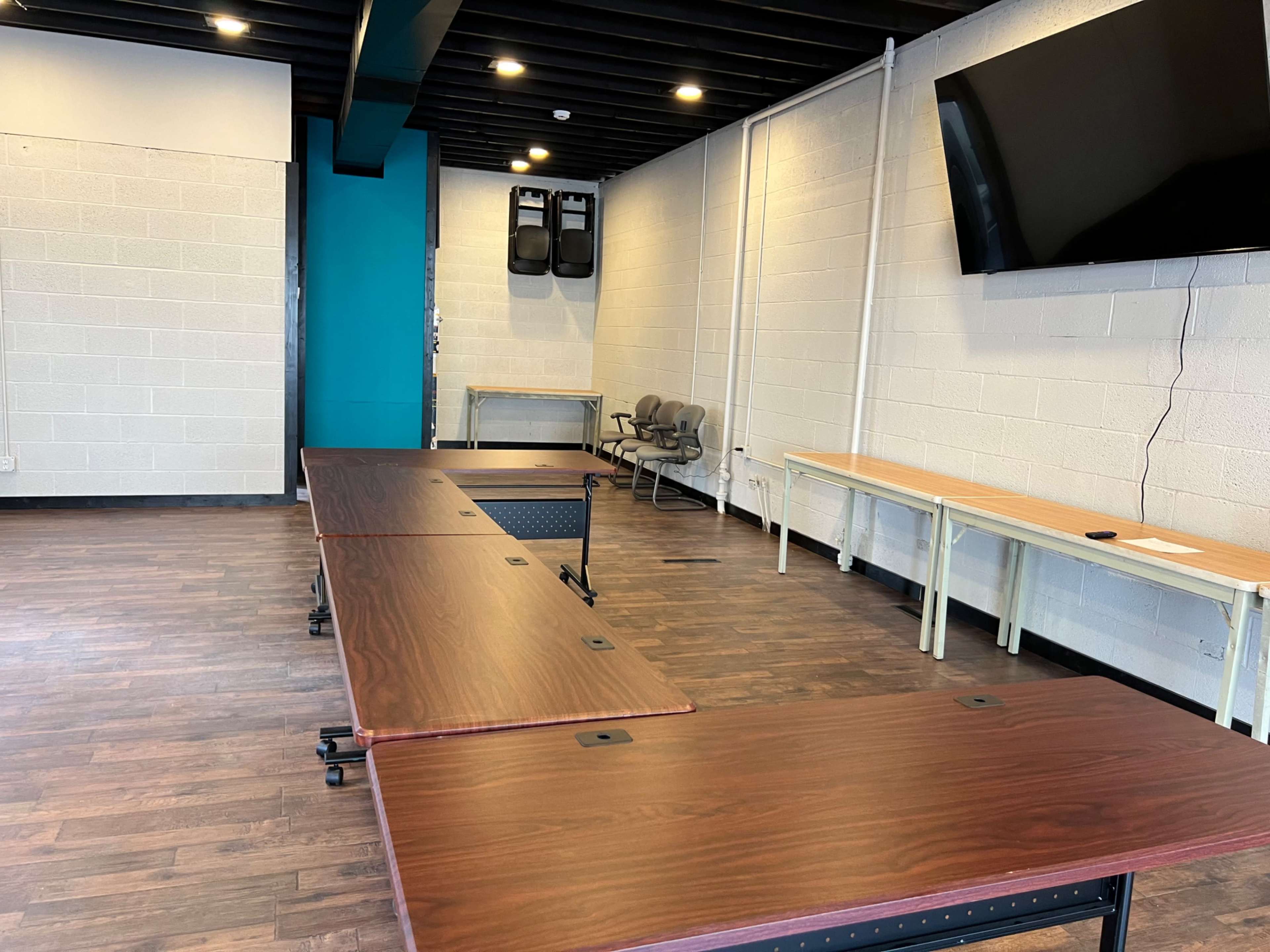 A meeting room with several tables arranged in a rectangular formation and a large flat-screen TV mounted on the wall.