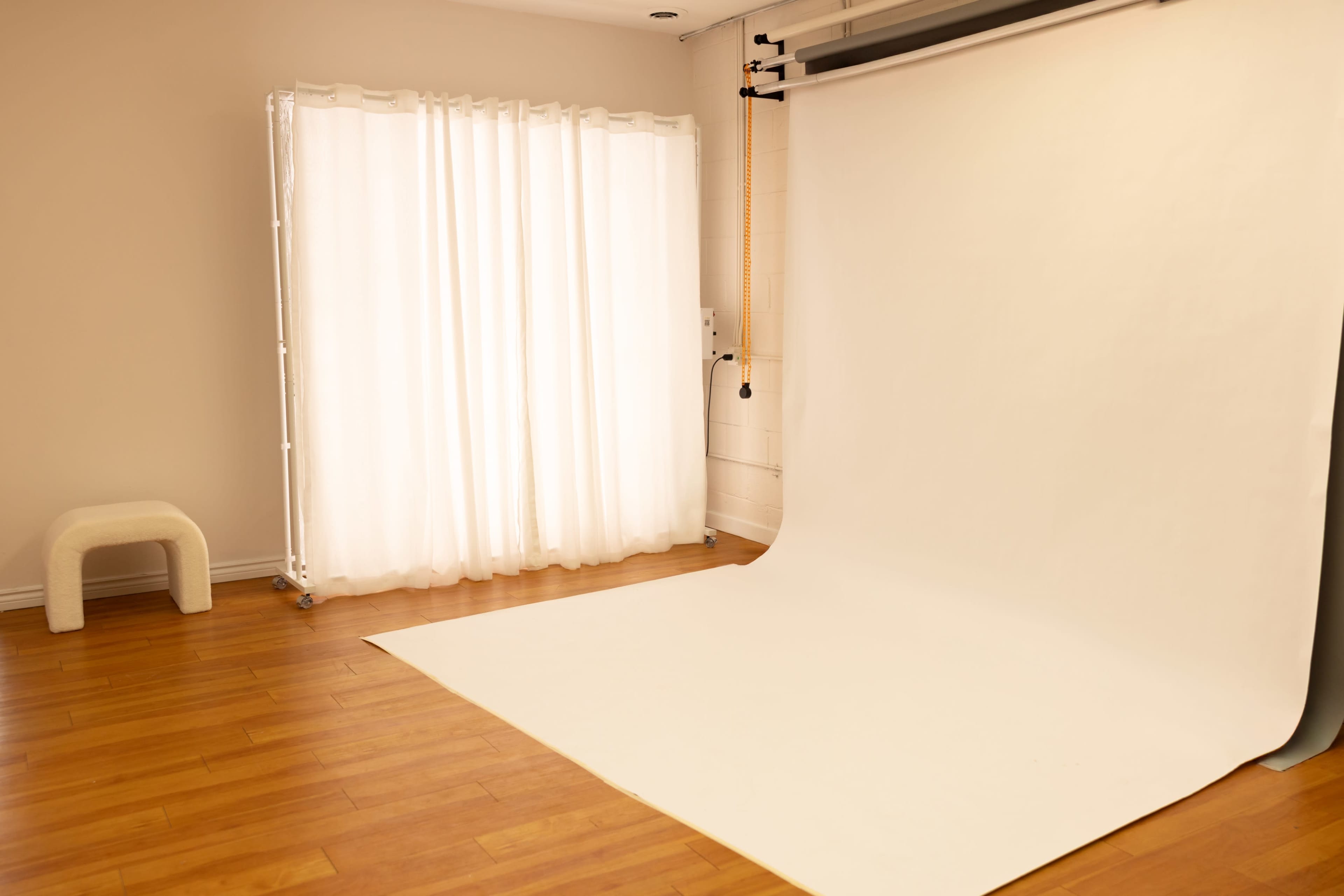 The image shows a photography studio with a large white backdrop, light wood flooring, and sheer curtains filtering natural light.