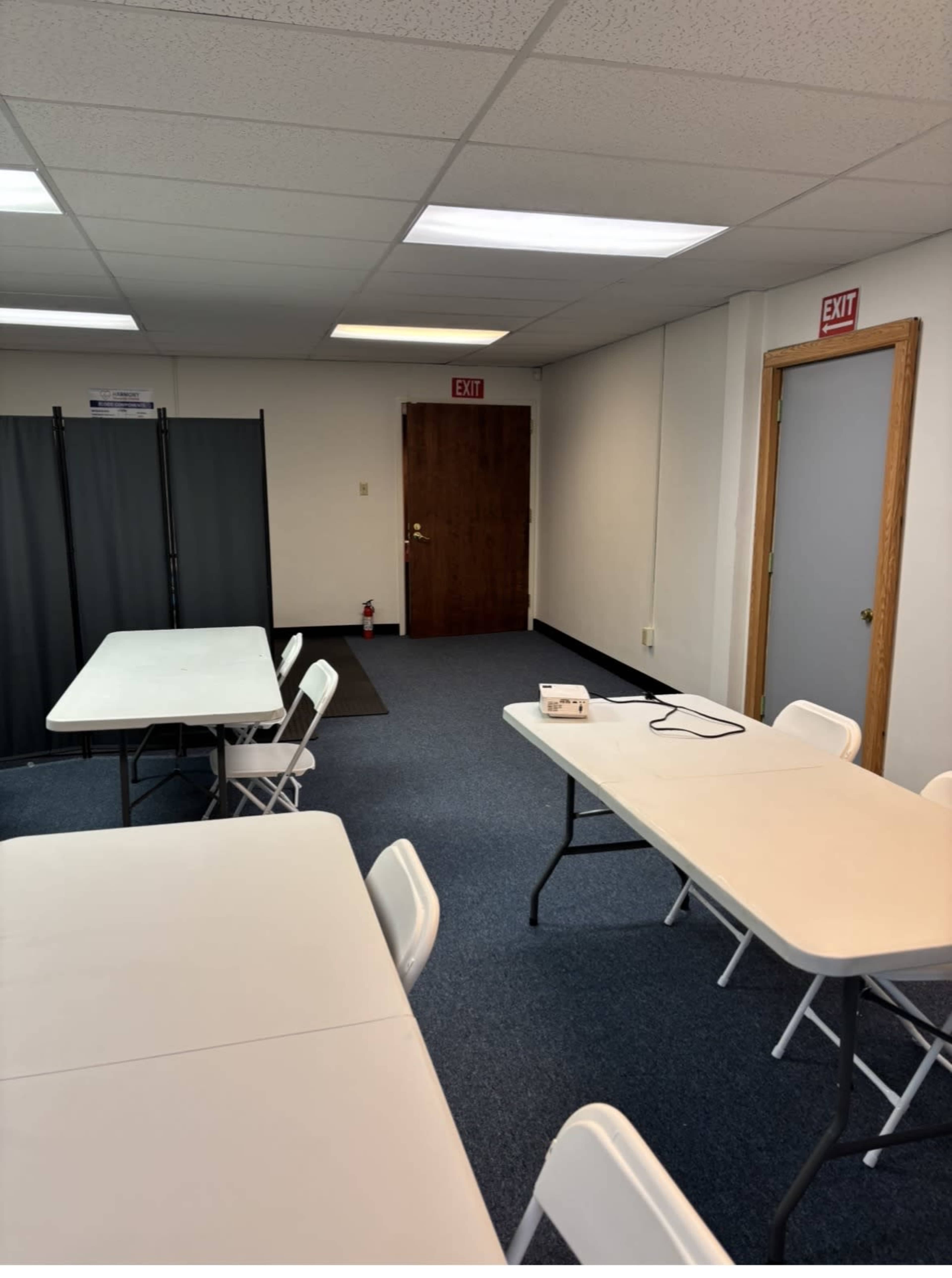 The image shows a business room with several tables and chairs set up, a pair of doors in the background, and a privacy screen on the left.