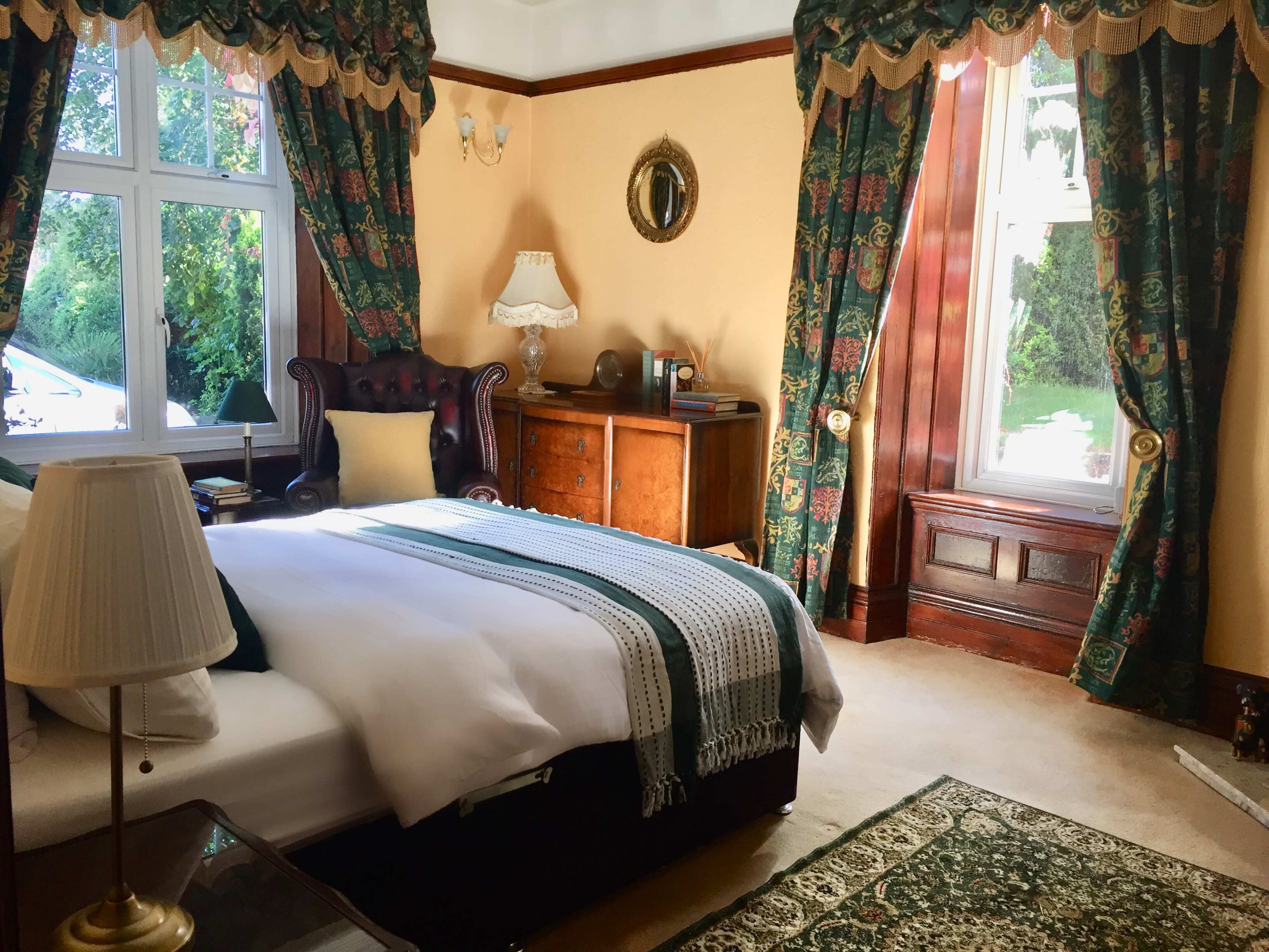 A classic bedroom featuring a large bed with white linens, ornate curtains, and wooden furniture.