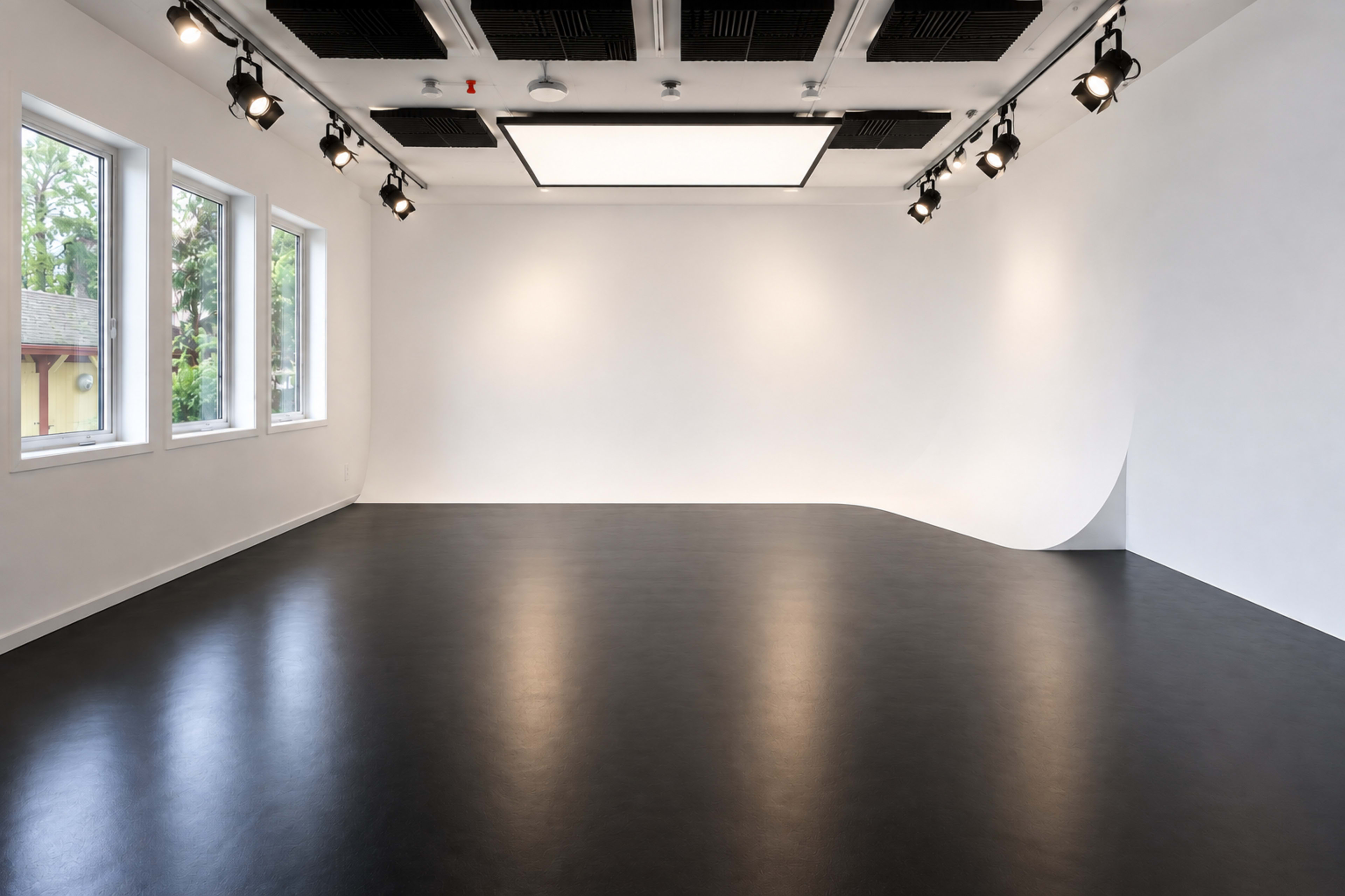 The image shows a modern, minimalist studio space with a curved white backdrop, black flooring, and multiple ceiling lights.