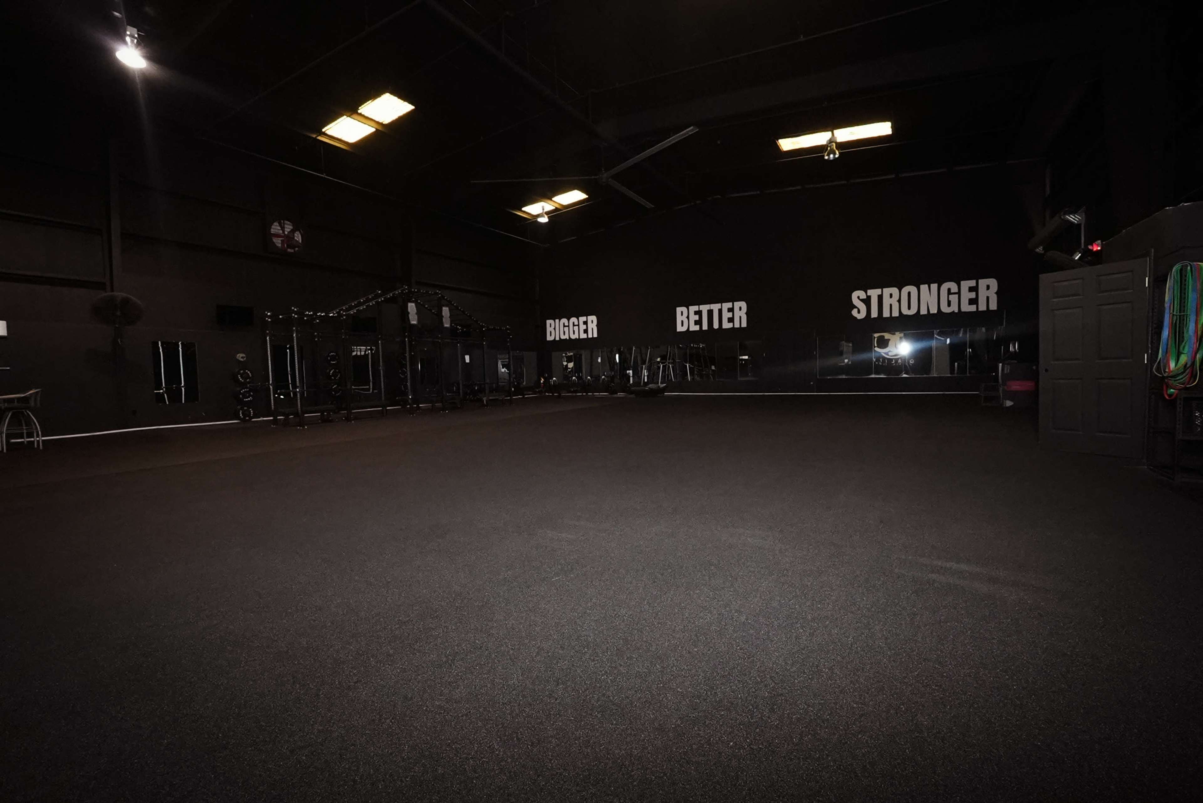 The image shows an empty gym with a black rubber floor and motivational phrases on the wall.