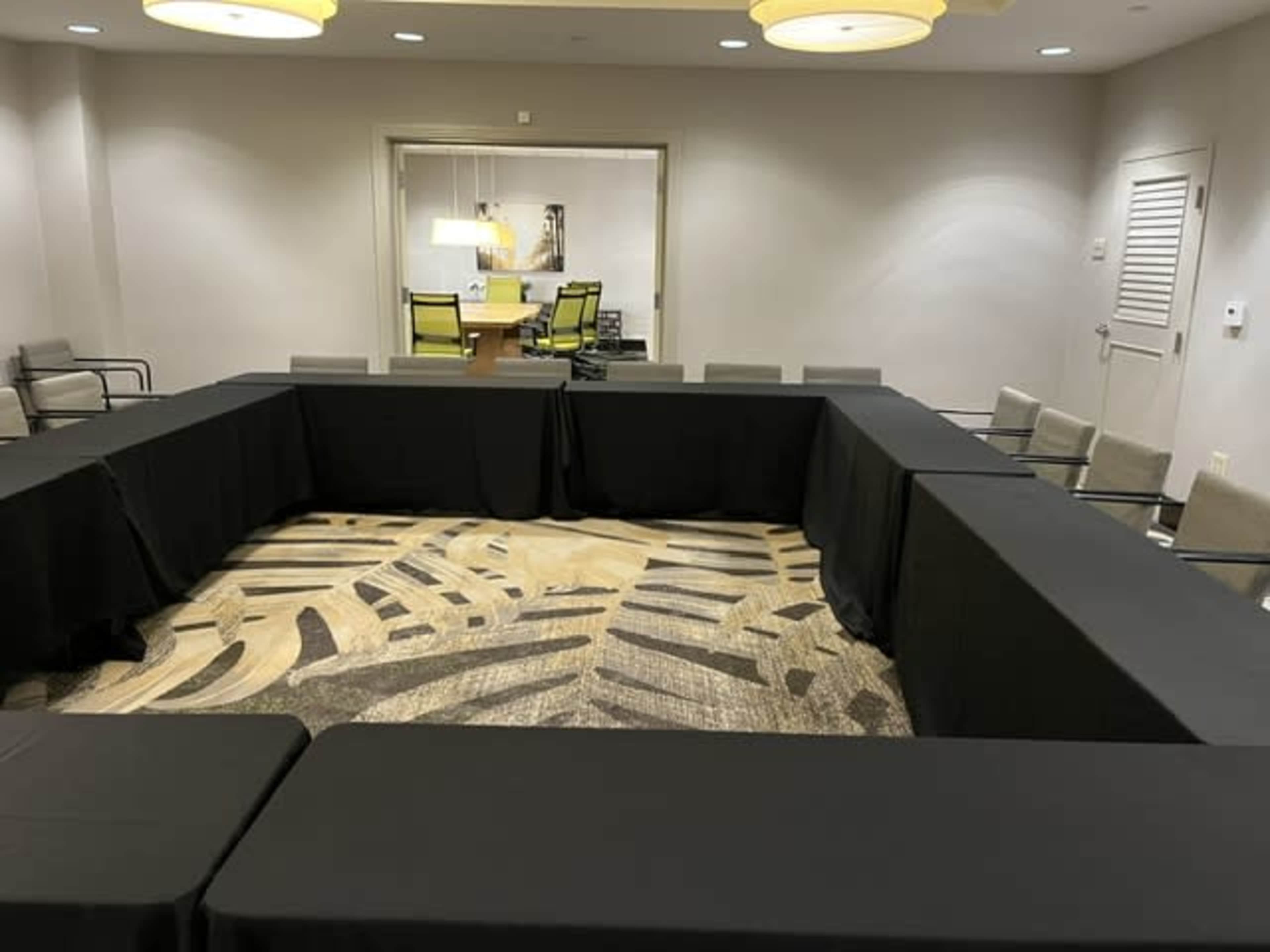 The image shows a conference room set up with a large U-shaped arrangement of tables covered in black tablecloths, surrounded by chairs.