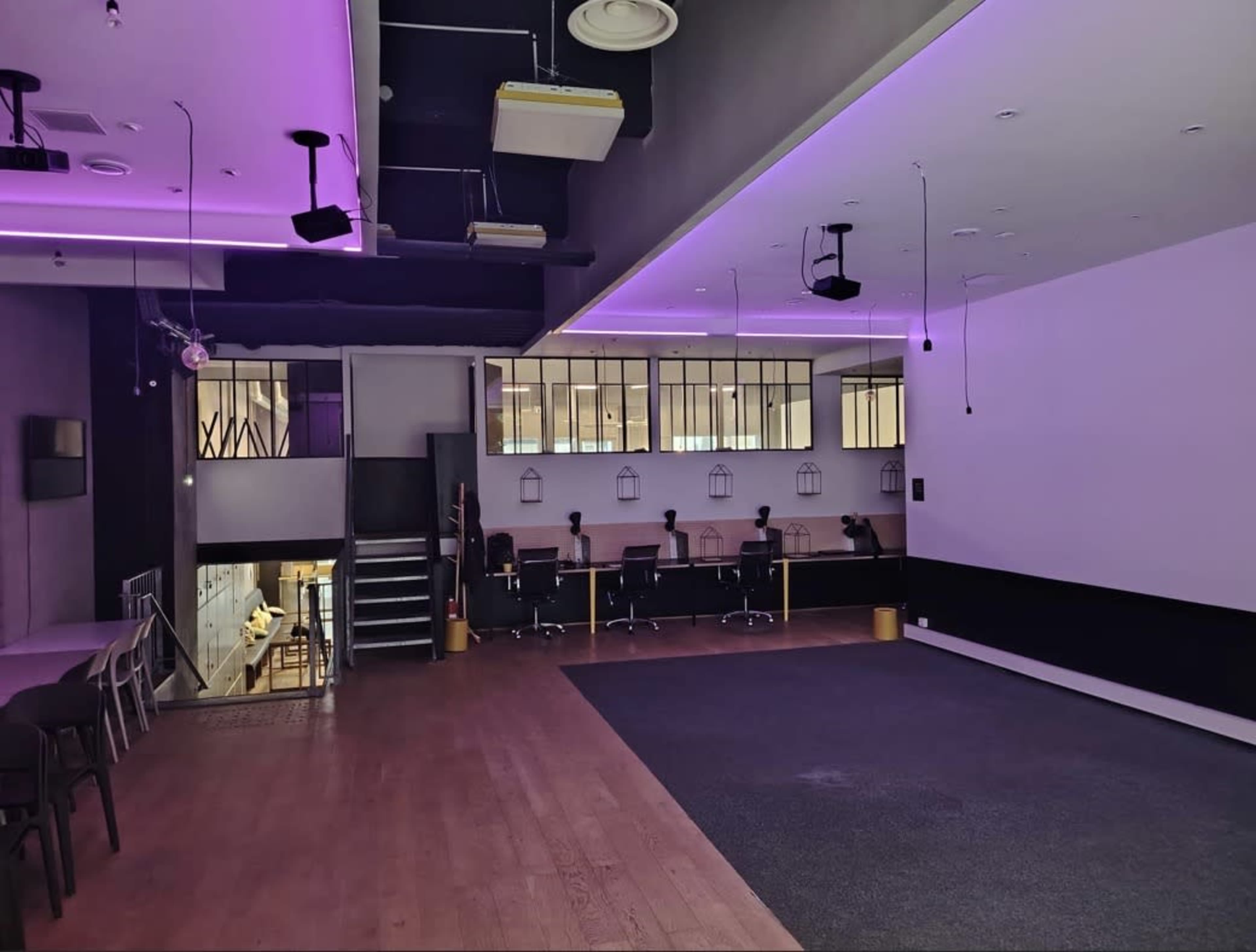 The image shows a modern, empty interior space with purple LED lighting, featuring a seating area and a section with office-style workstations.