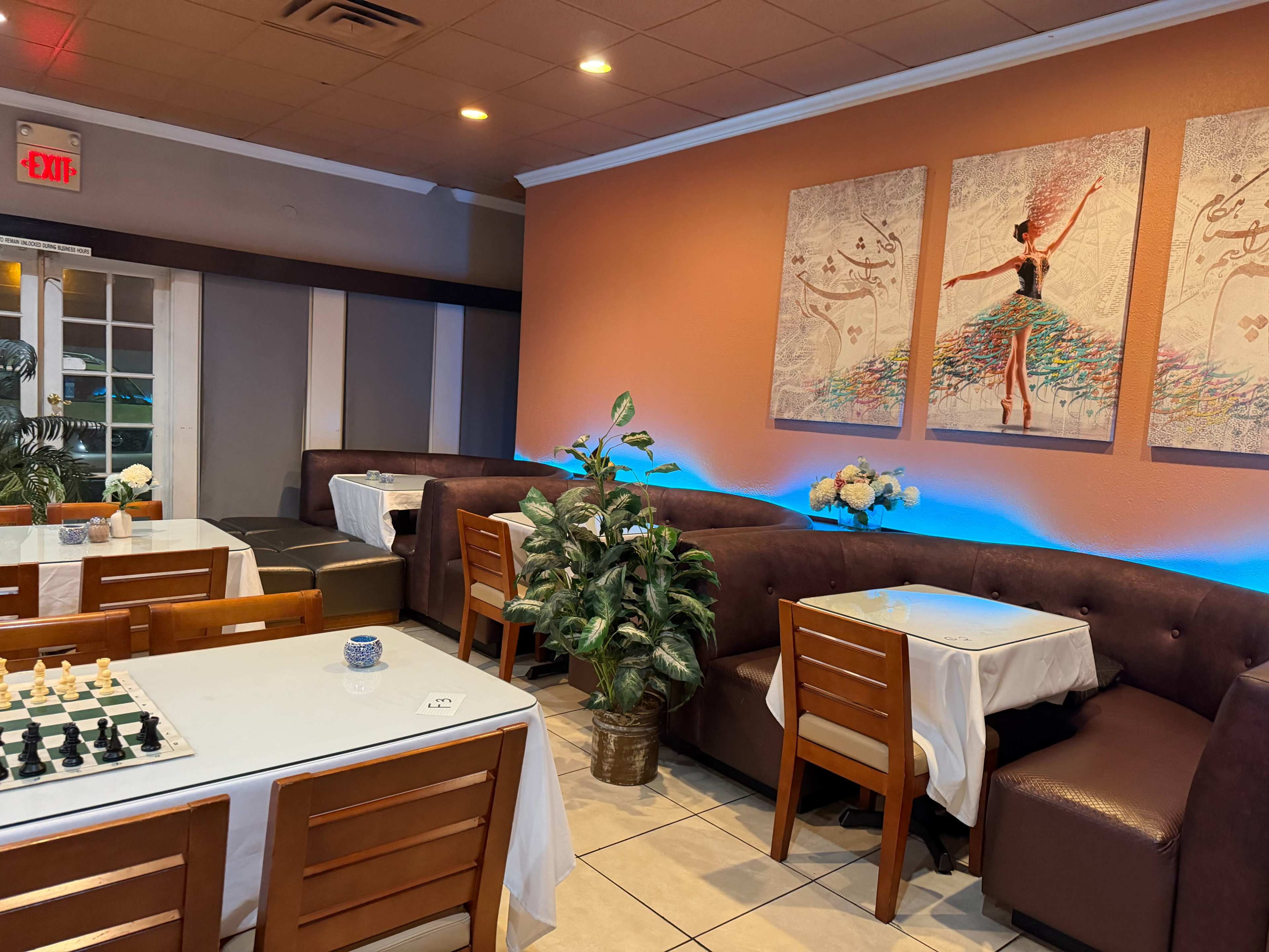 The image shows a cozy restaurant interior with brown booth seating, white tablecloths on tables, a chessboard on one table, and art featuring a dancer on the walls.