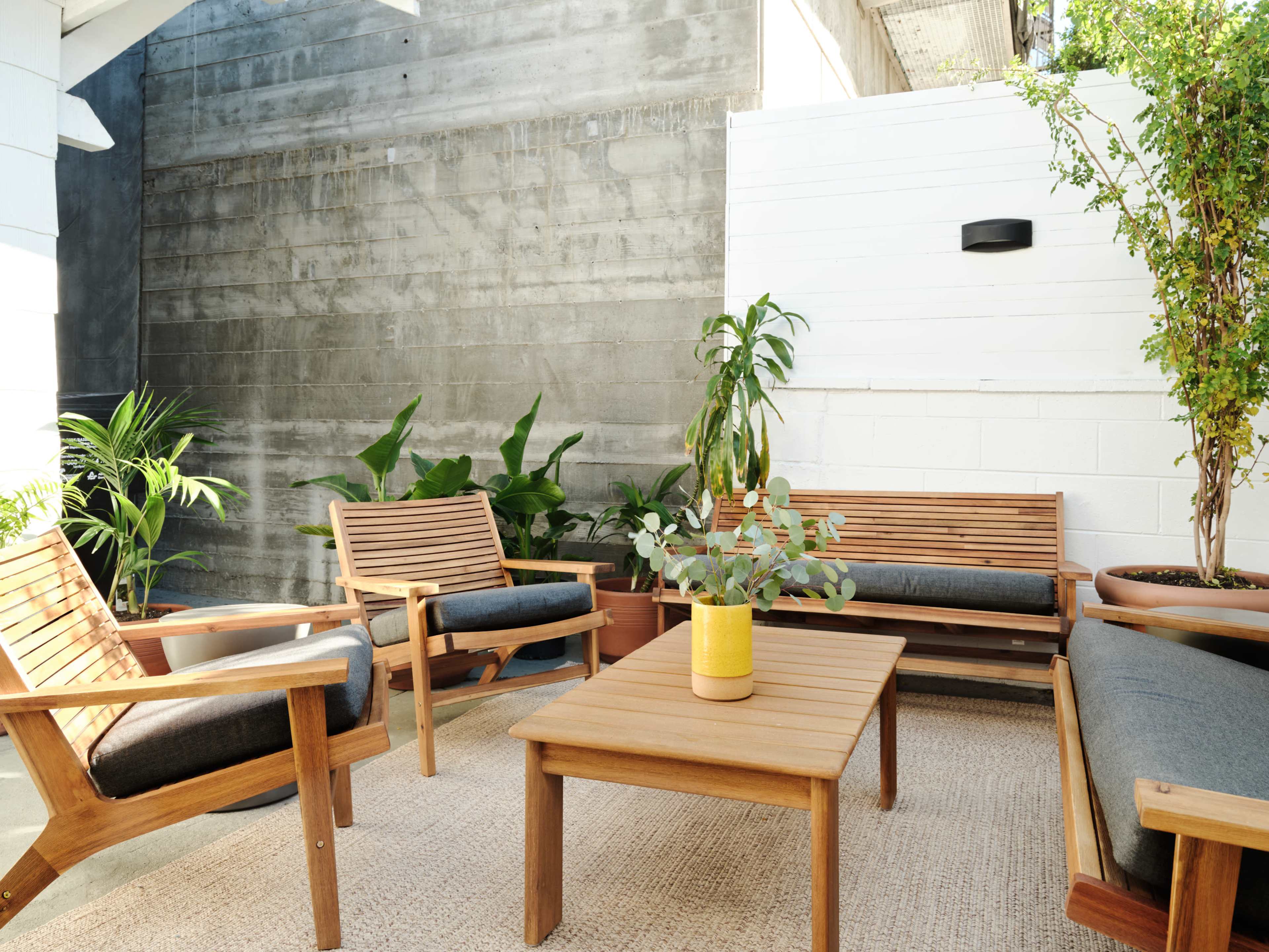 A modern outdoor seating area with wooden furniture, a small table, and potted plants against a concrete wall.