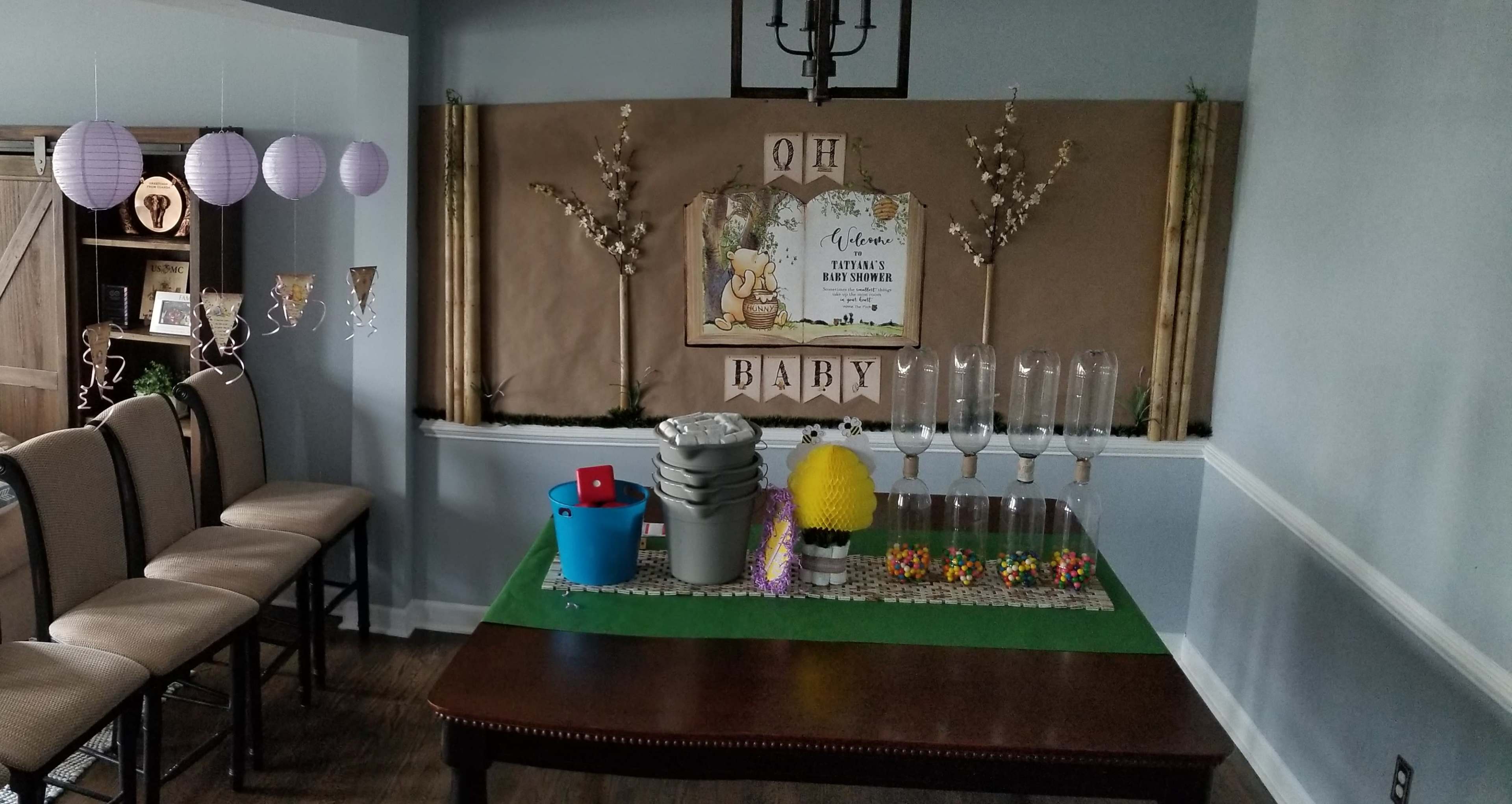 A decorated room features a table with colorful party supplies and a 'Oh Baby' sign, surrounded by chairs and wall decorations.