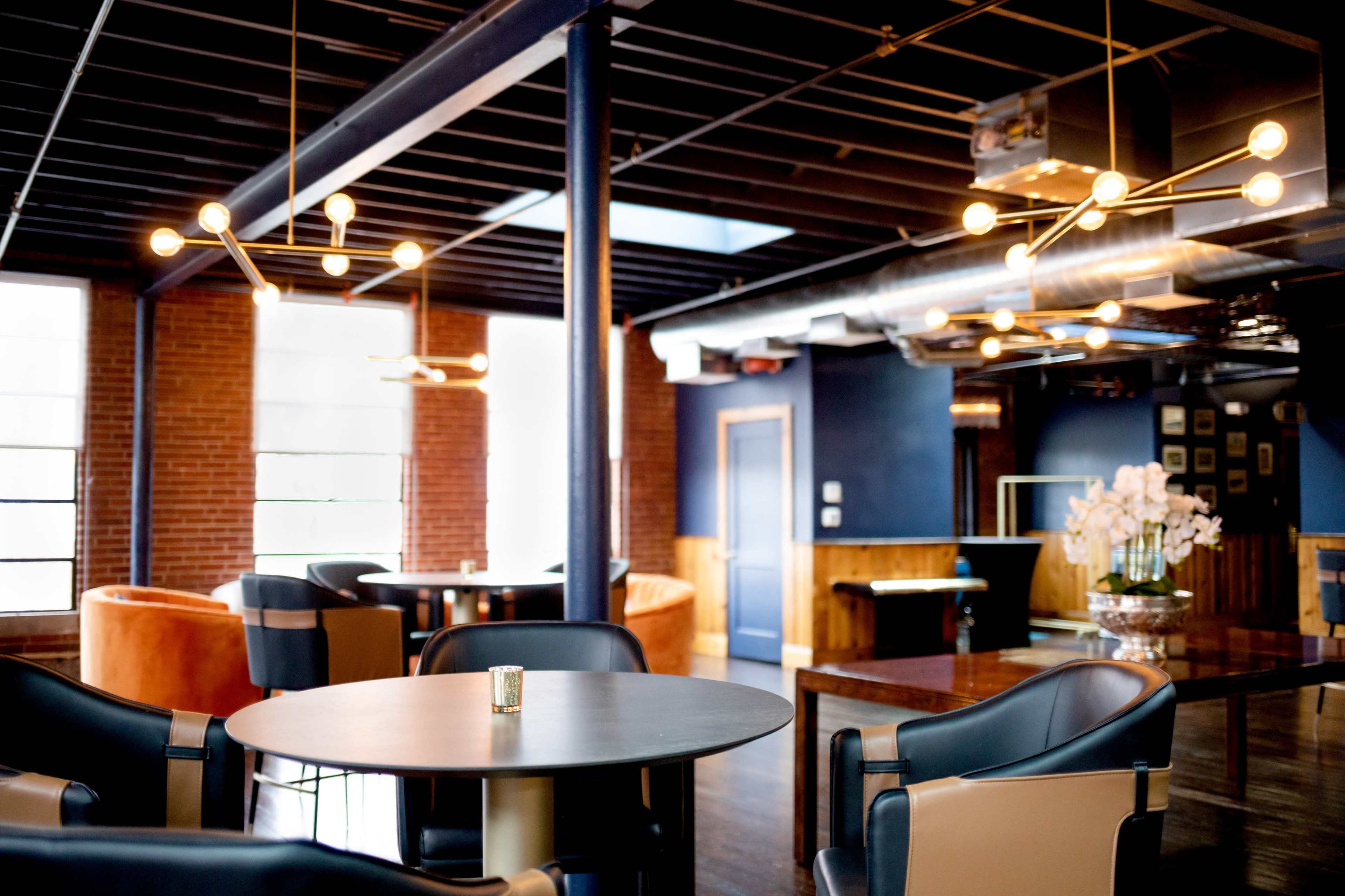 A modern dining area with stylish furniture, including a round table and upholstered chairs, illuminated by contemporary lighting fixtures.