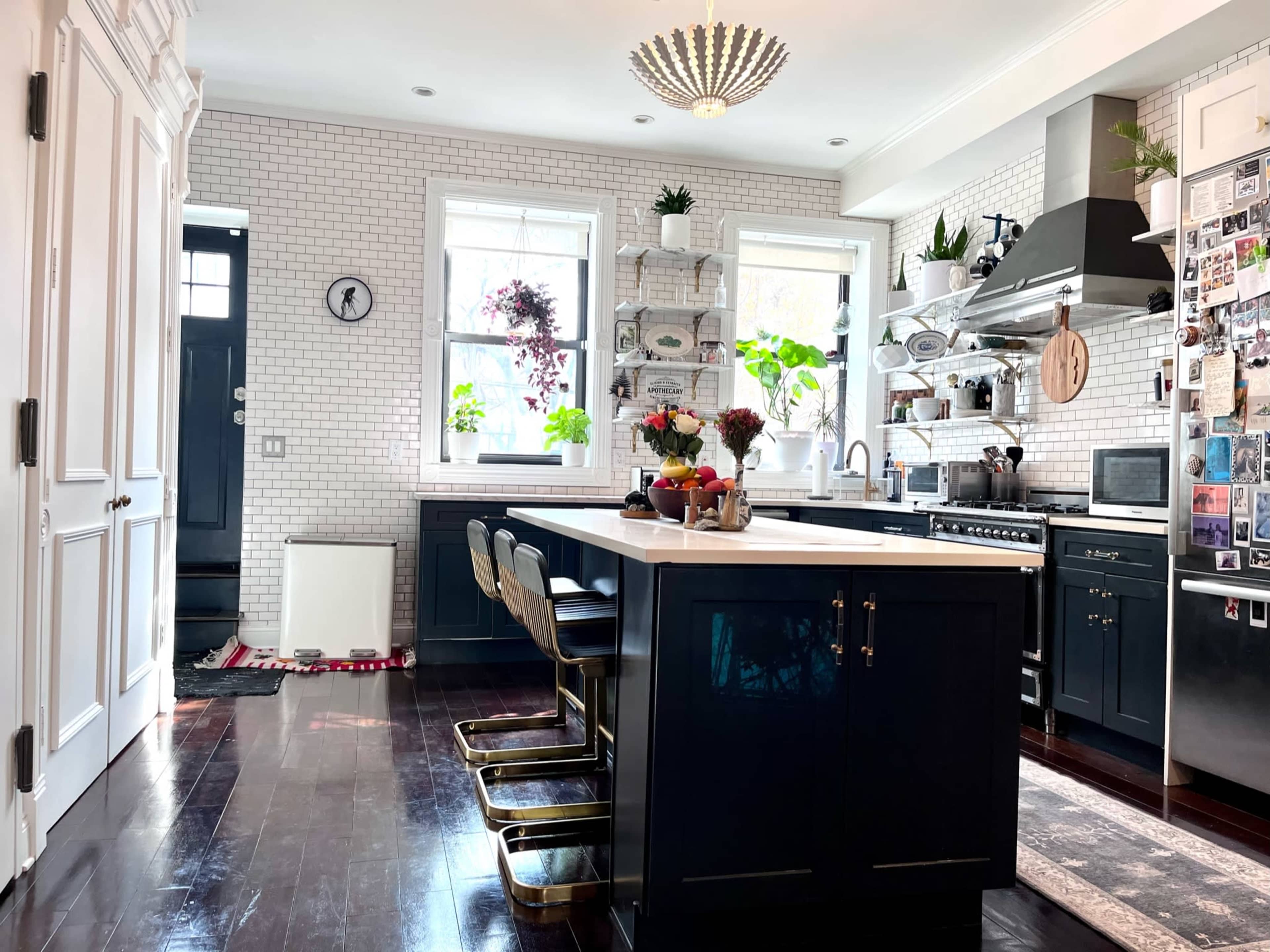 A modern kitchen features a large island with bar stools, stainless steel appliances, and white subway tile on the walls.