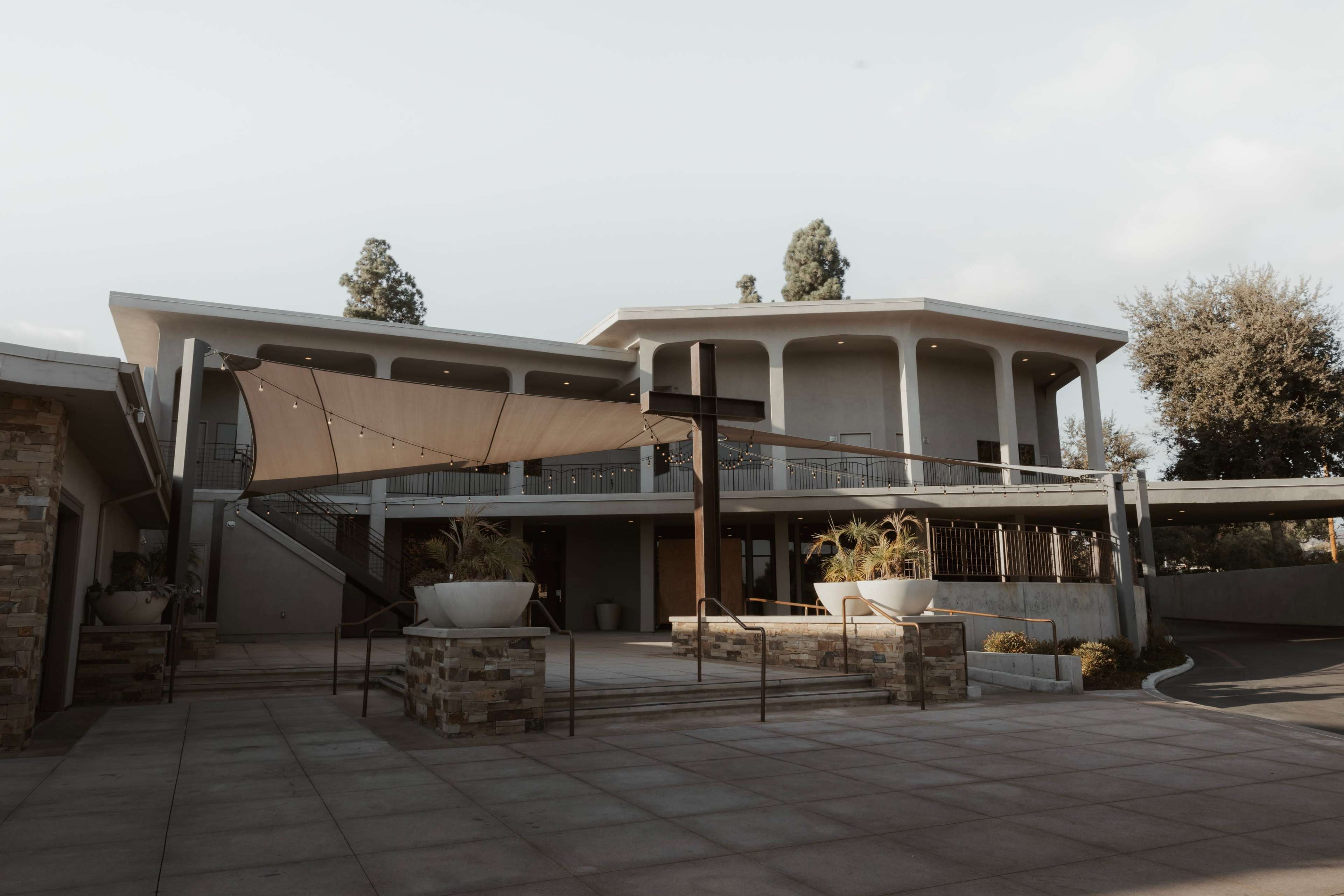 The image shows a modern building with a large covered area and outdoor seating, surrounded by well-maintained landscaping.