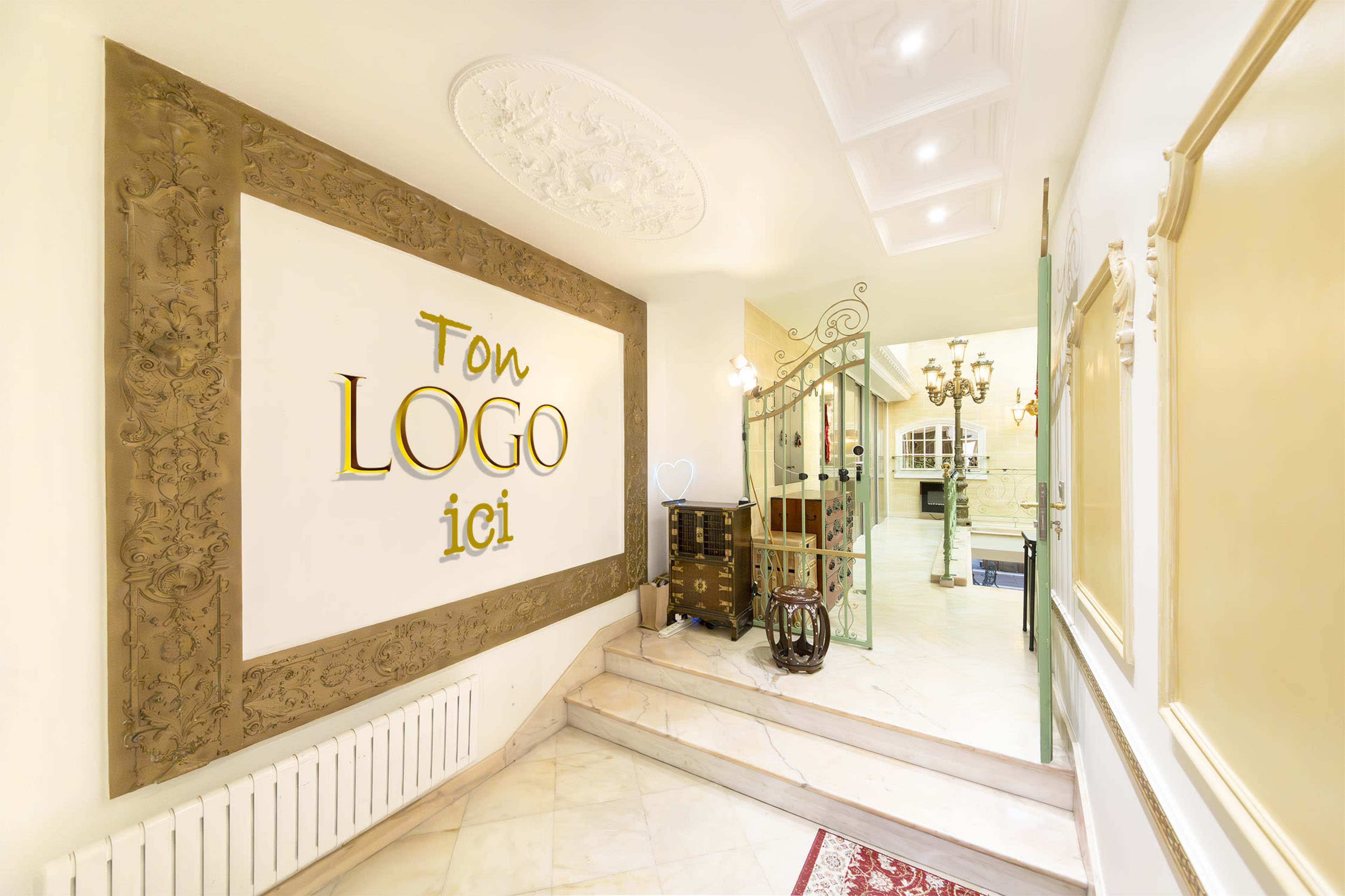 An elegant entrance hall with a decorative wall featuring the words "Ton LOGO ici," along with a staircase leading to another area and ornate light fixtures in the background.
