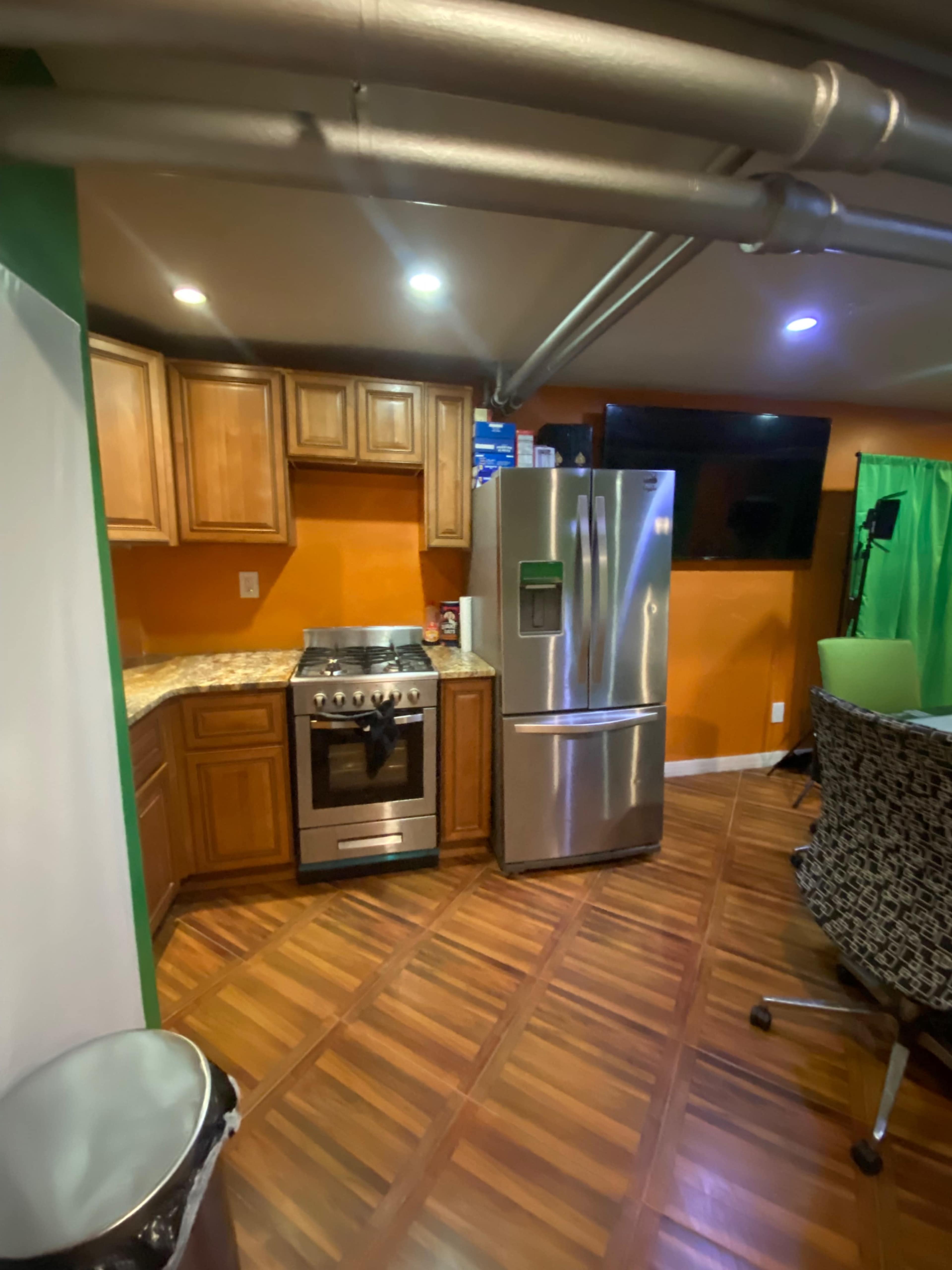 A kitchen with wooden cabinets, a stainless steel refrigerator, a gas stove, and a wooden floor in an orange-painted room.