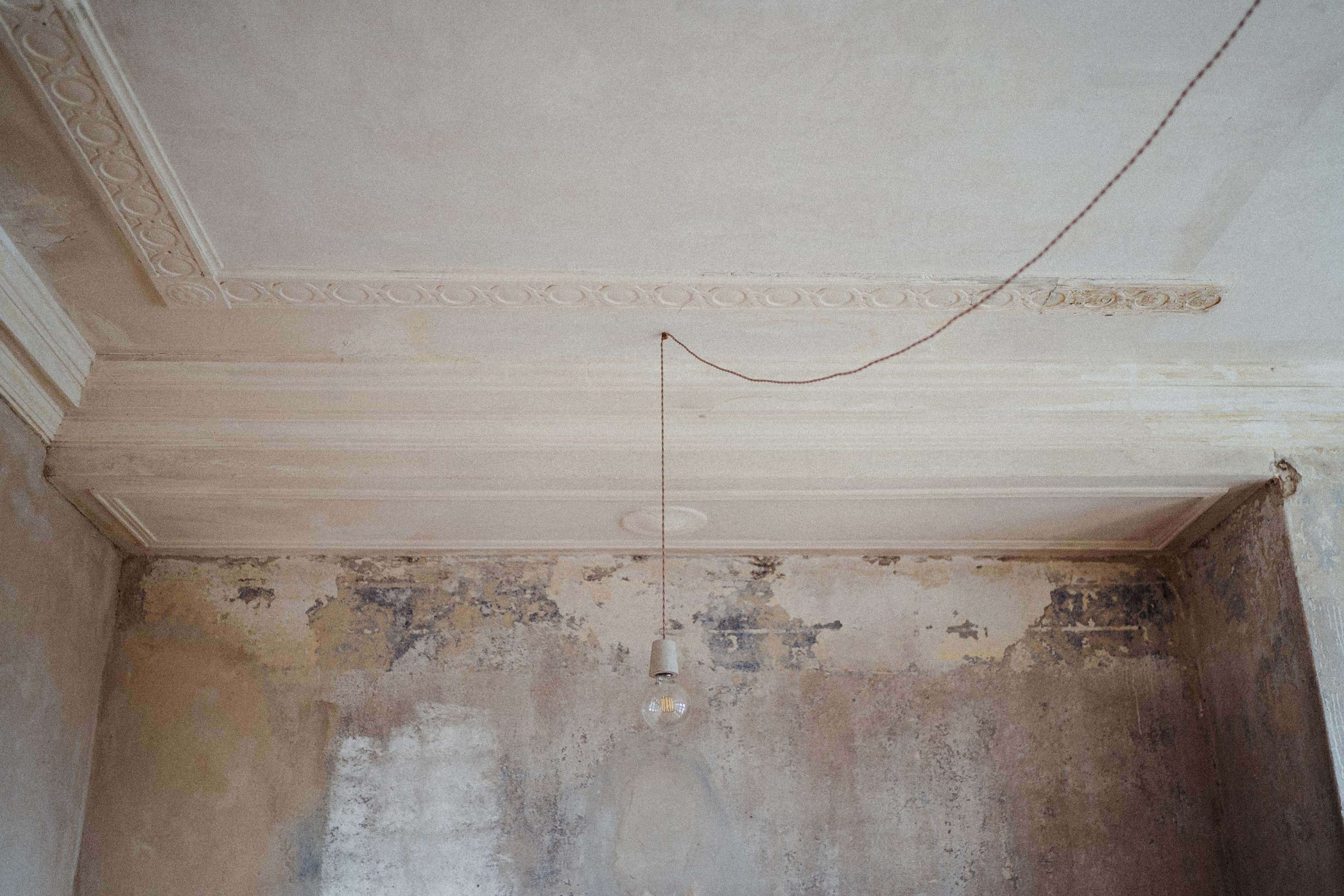 A bare room with peeling walls and a single light bulb hanging from the ceiling.